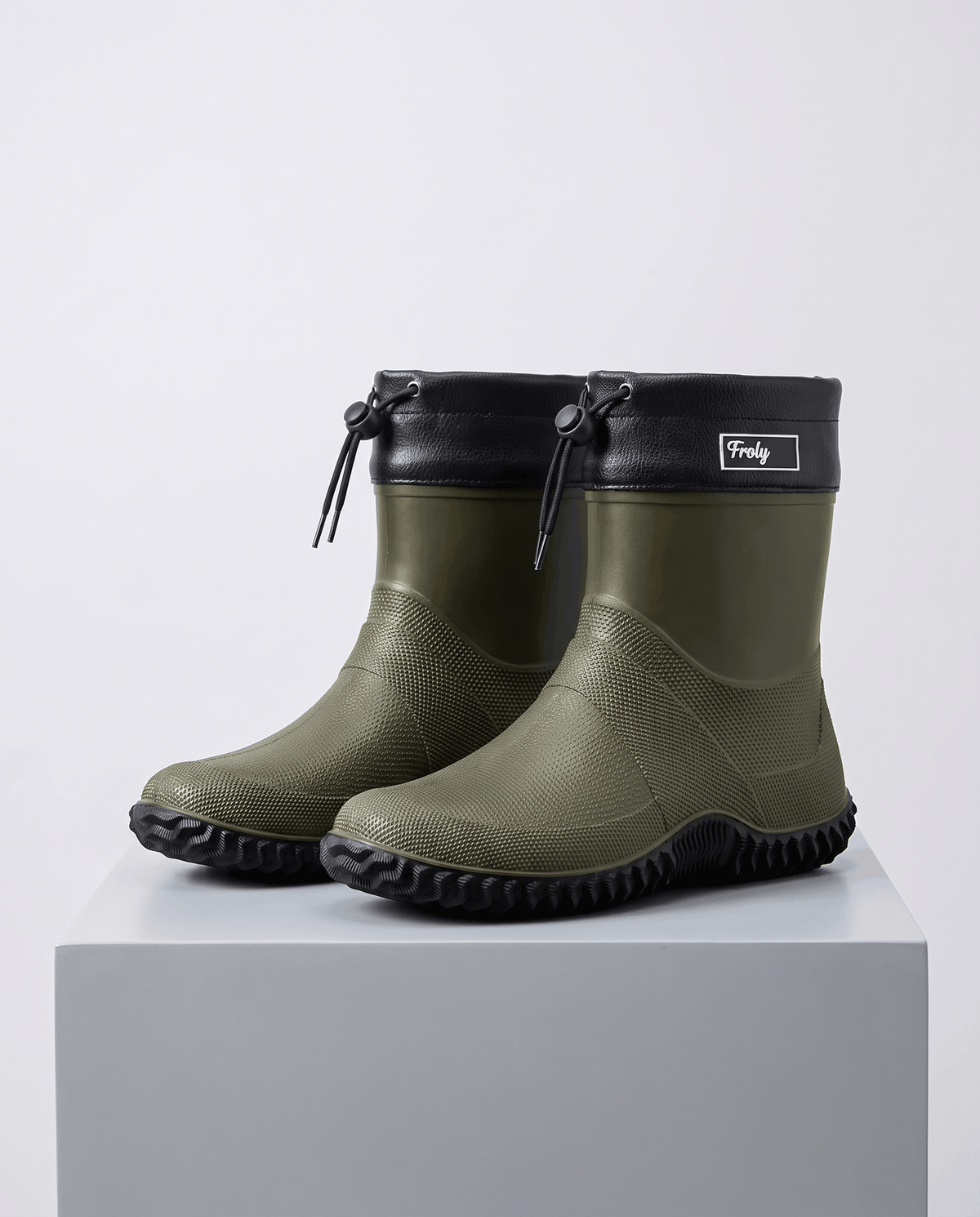 Pair of men's rubber work boots in army green with black drawstring collars on a grey block