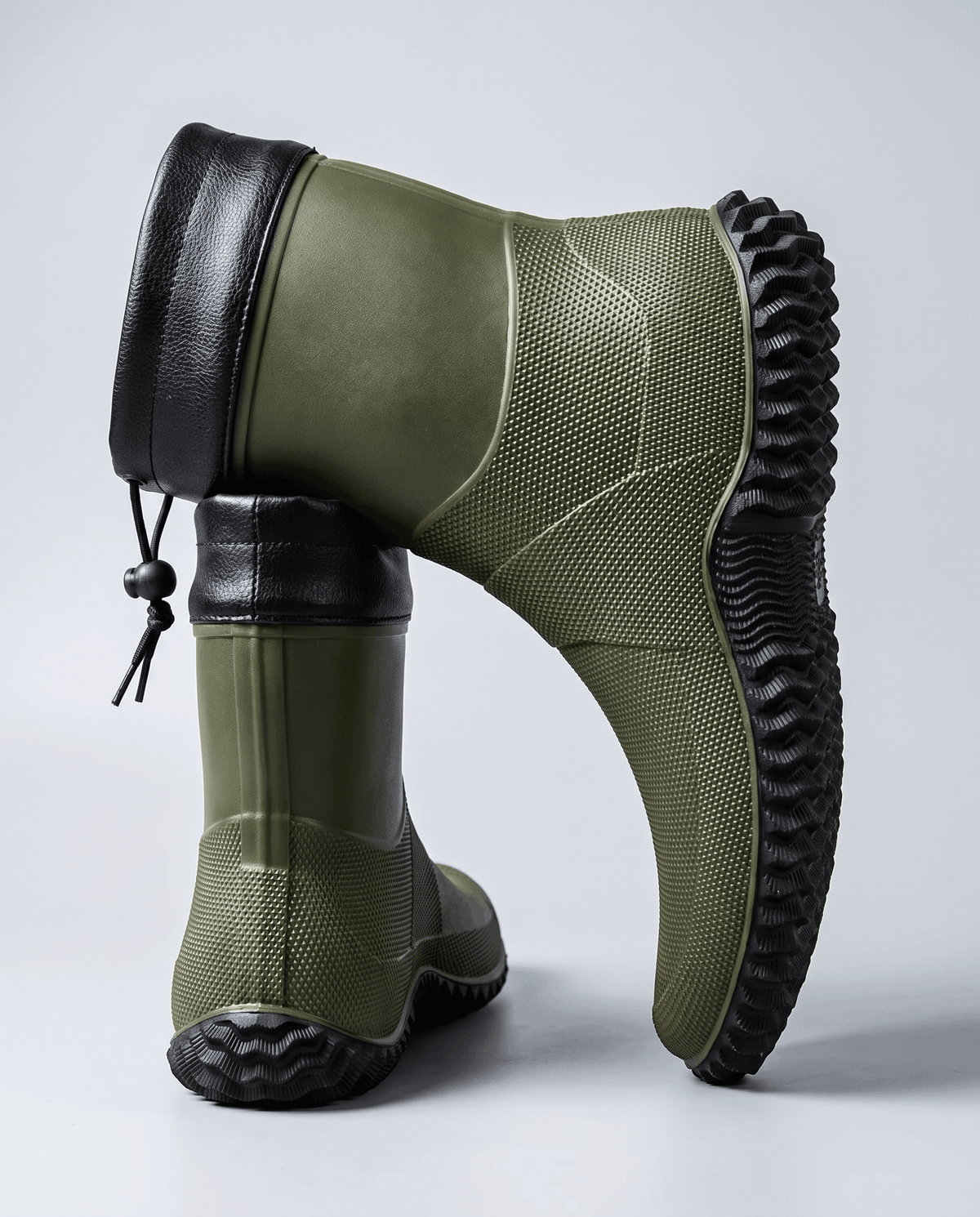 Army green boots with deep lug soles, one tilted to show the tread