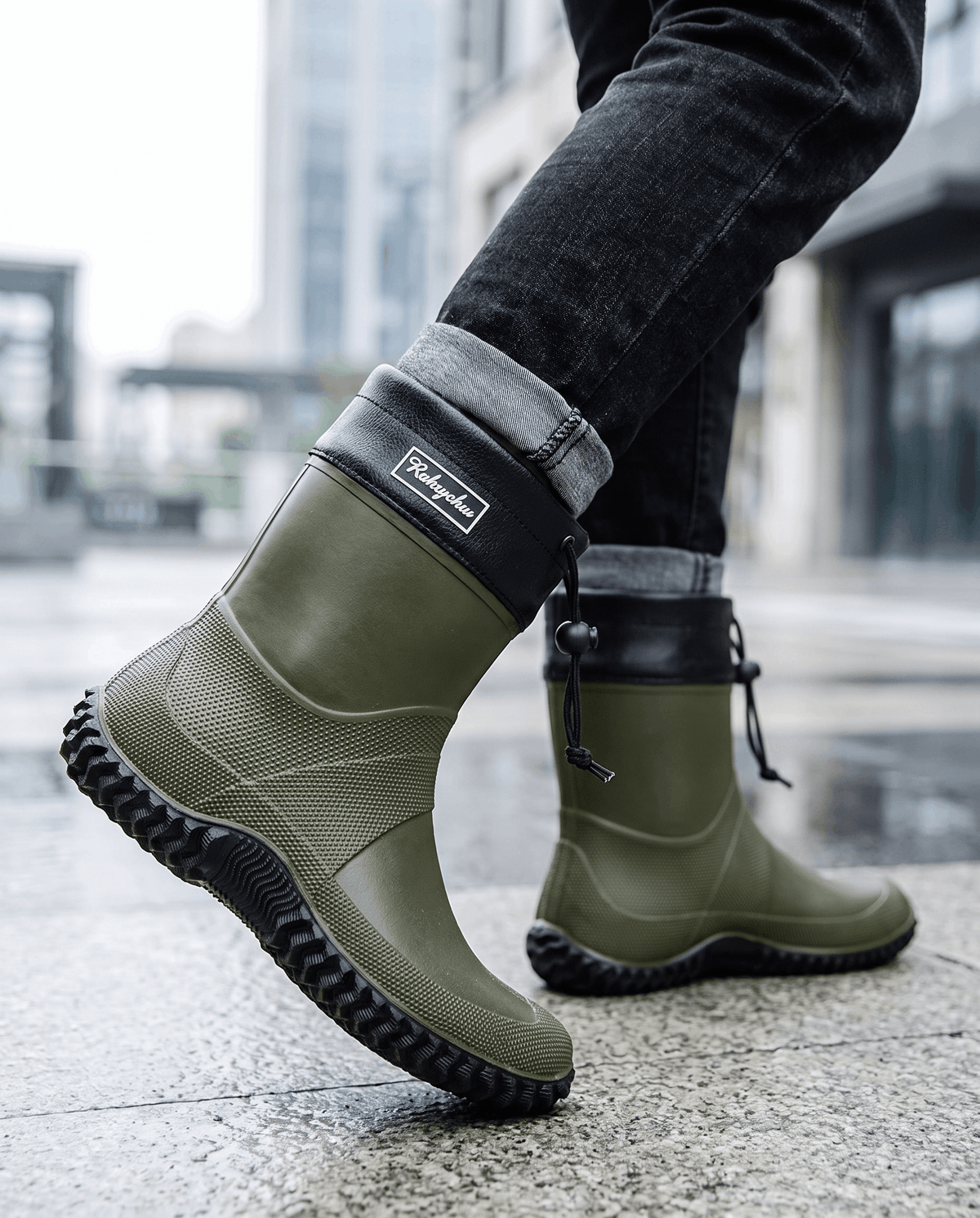 Legs in dark jeans walking in army green rubber boots on wet pavement