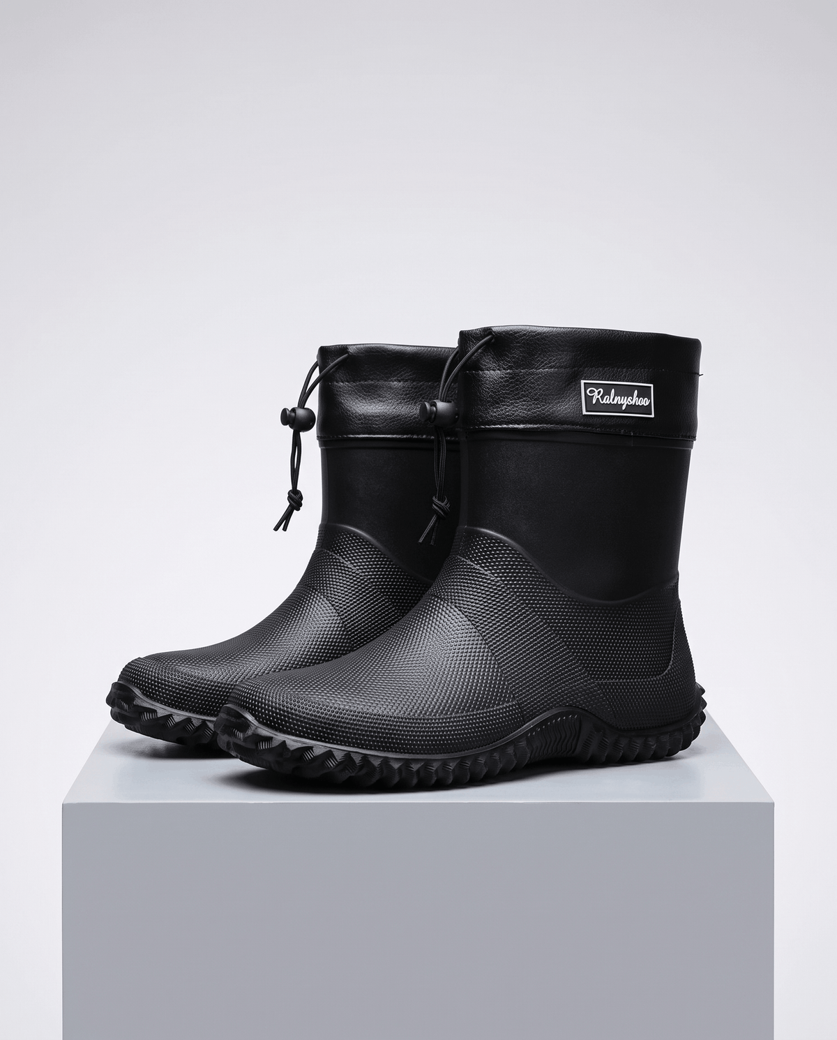 Pair of black rubber boots with drawstring collars standing on a grey block
