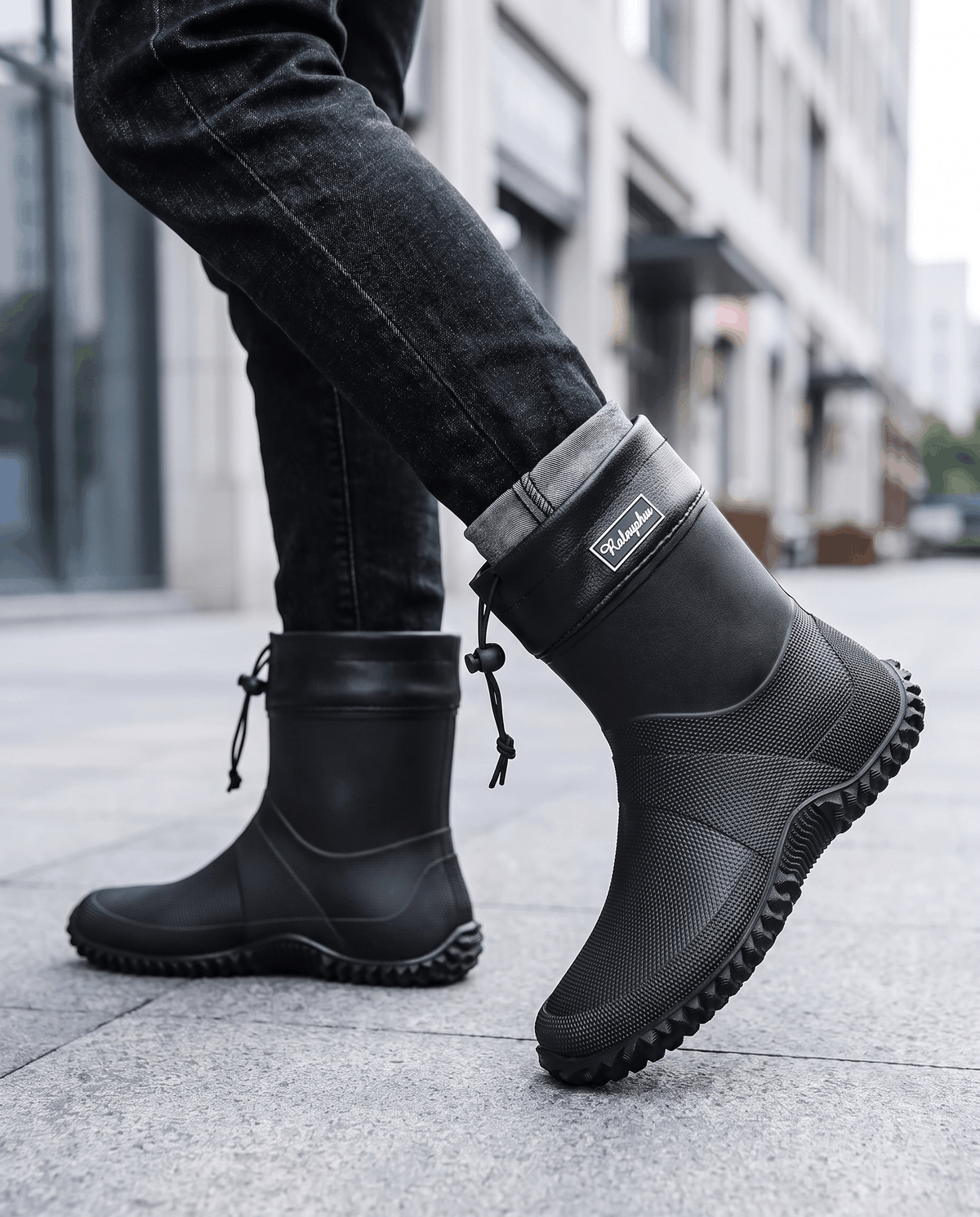 Man mid-stride in black rubber boots with dark jeans on a city street