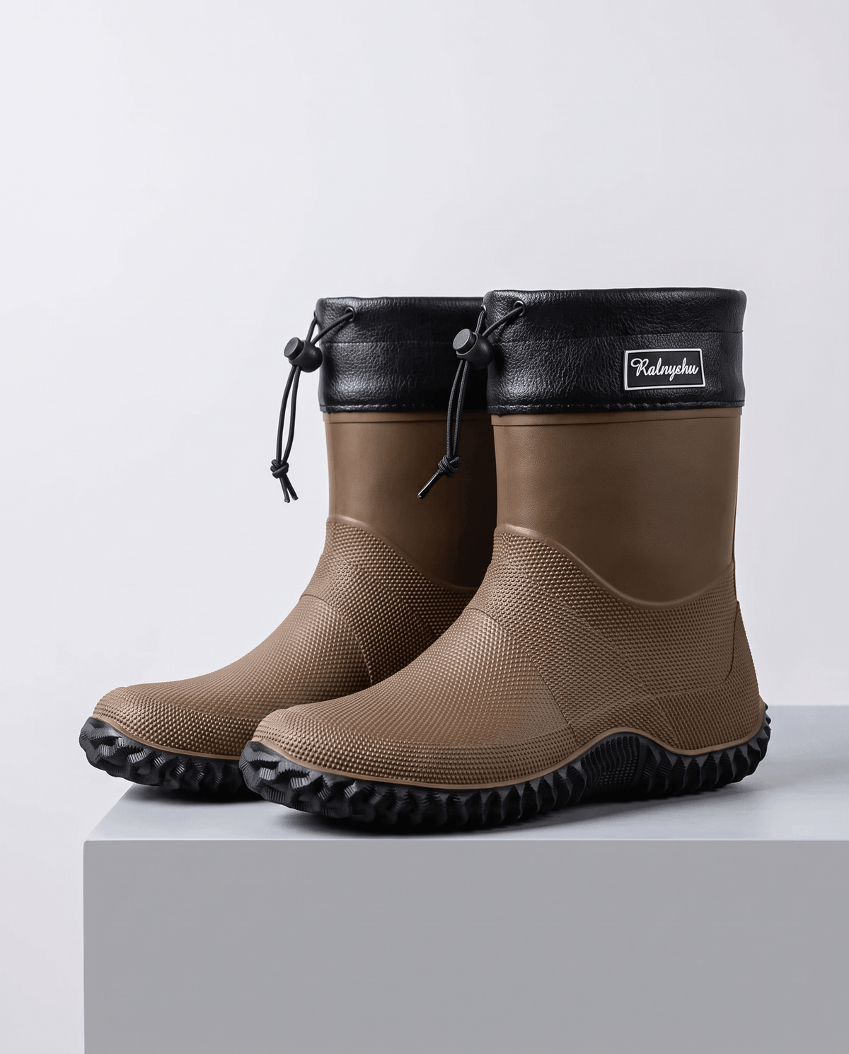 Pair of brown rubber boots with black collars on a grey block