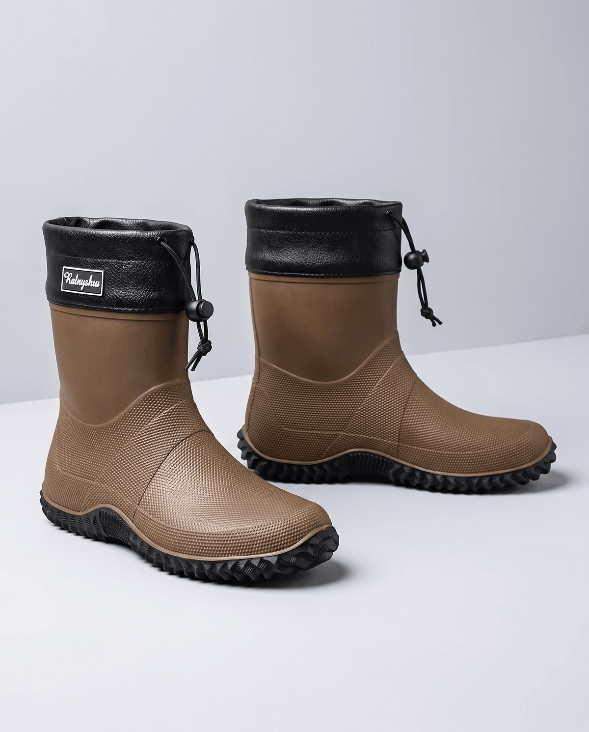 Two brown rubber boots with black drawstring collars and lug soles on grey
