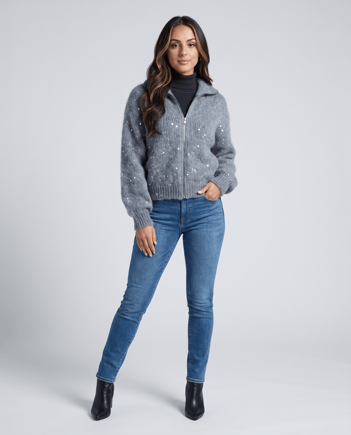 Model wearing the gray sequin cardigan zipped over a black turtleneck with blue jeans