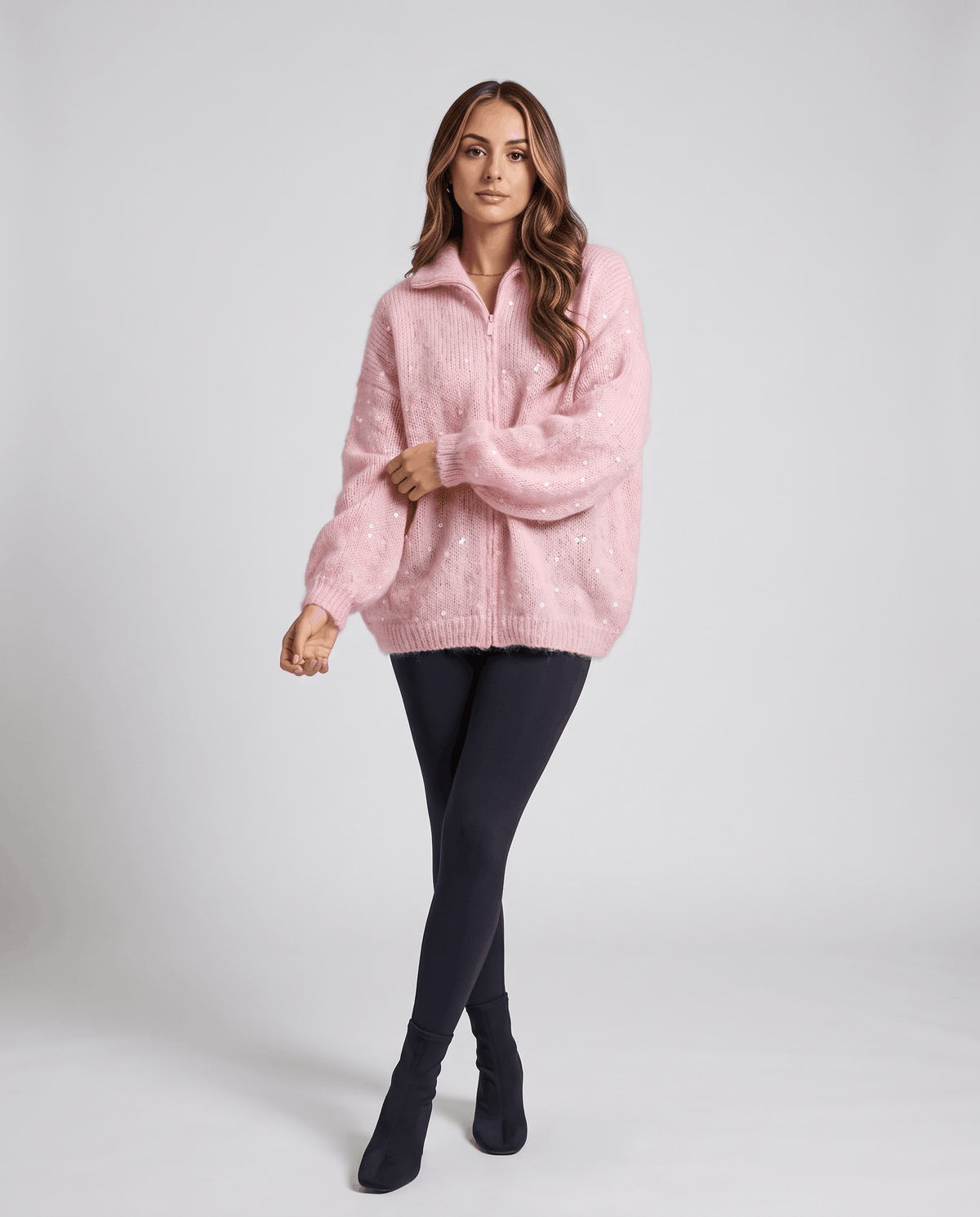 Model in the pink sparkly cardigan styled with navy leggings and black boots