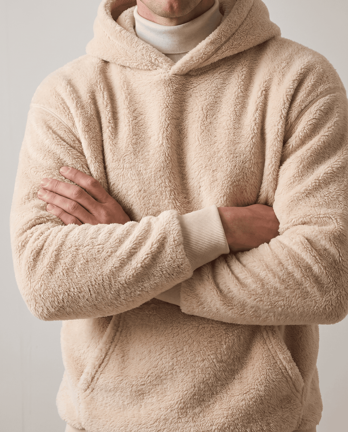 Beige hoodie worn over a white turtleneck with arms crossed