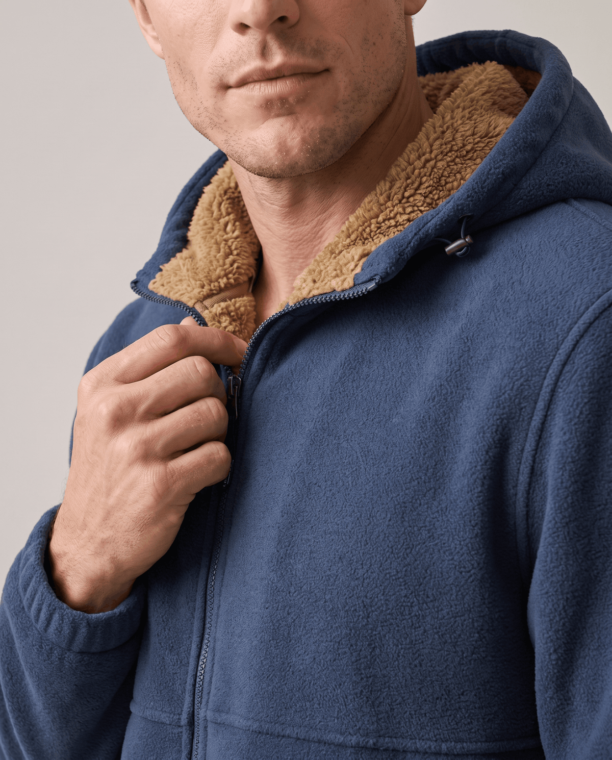 Close-up of a hand on the zip of the navy hoodie with sherpa-lined hood