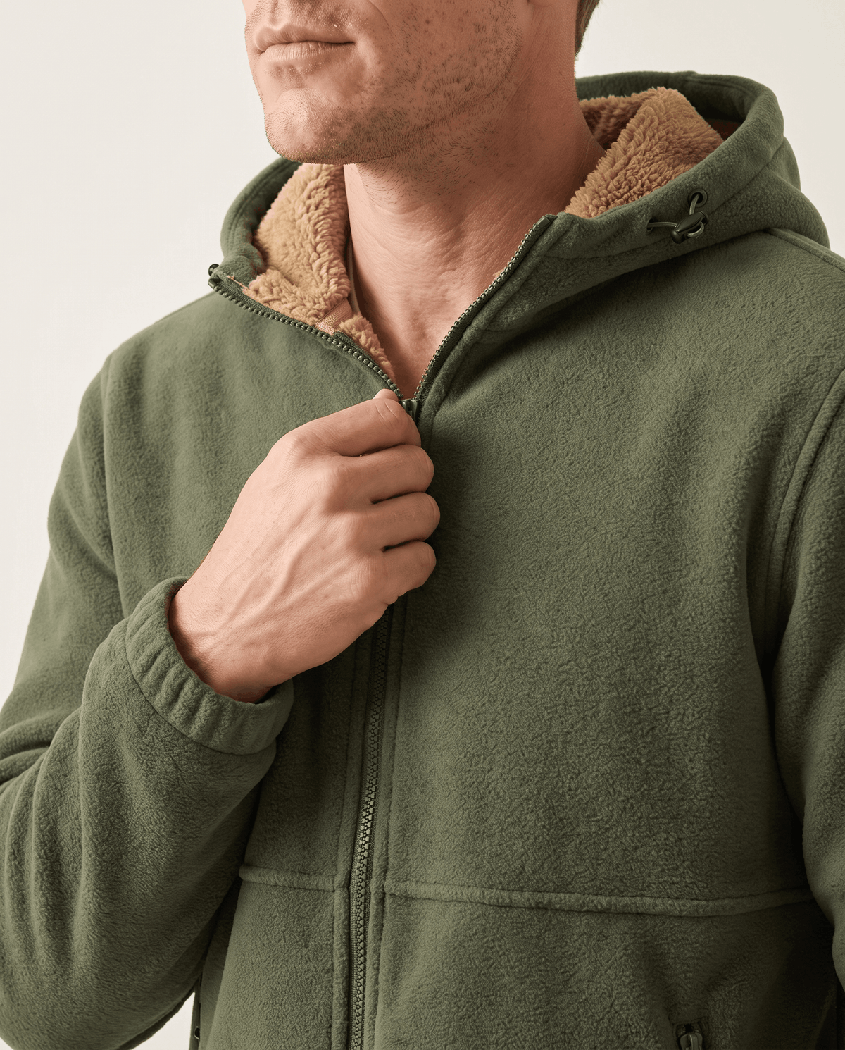 Close-up of a hand on the zip of the green fleece hoodie with sherpa-lined hood