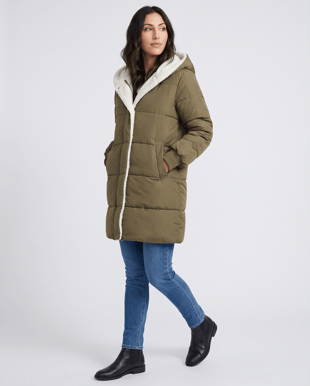 Model walking in army green coat with blue jeans and black boots
