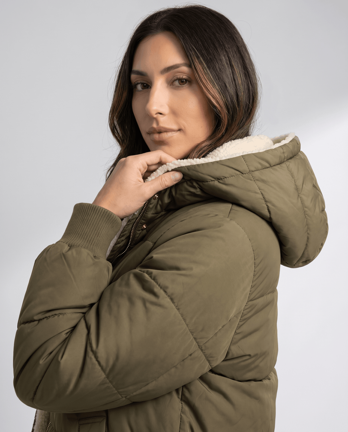 Model holding the sherpa hood of an army green puffer coat