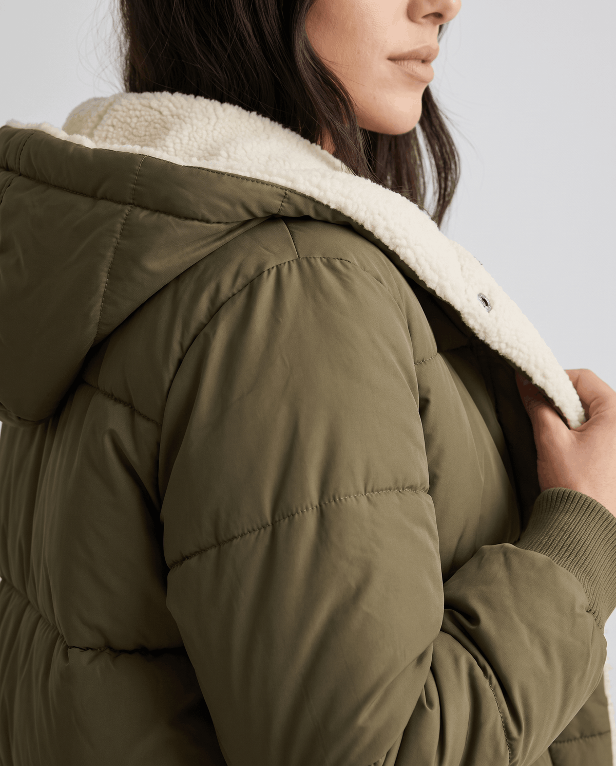 Close-up of army green coat with sherpa-lined hood and snap front