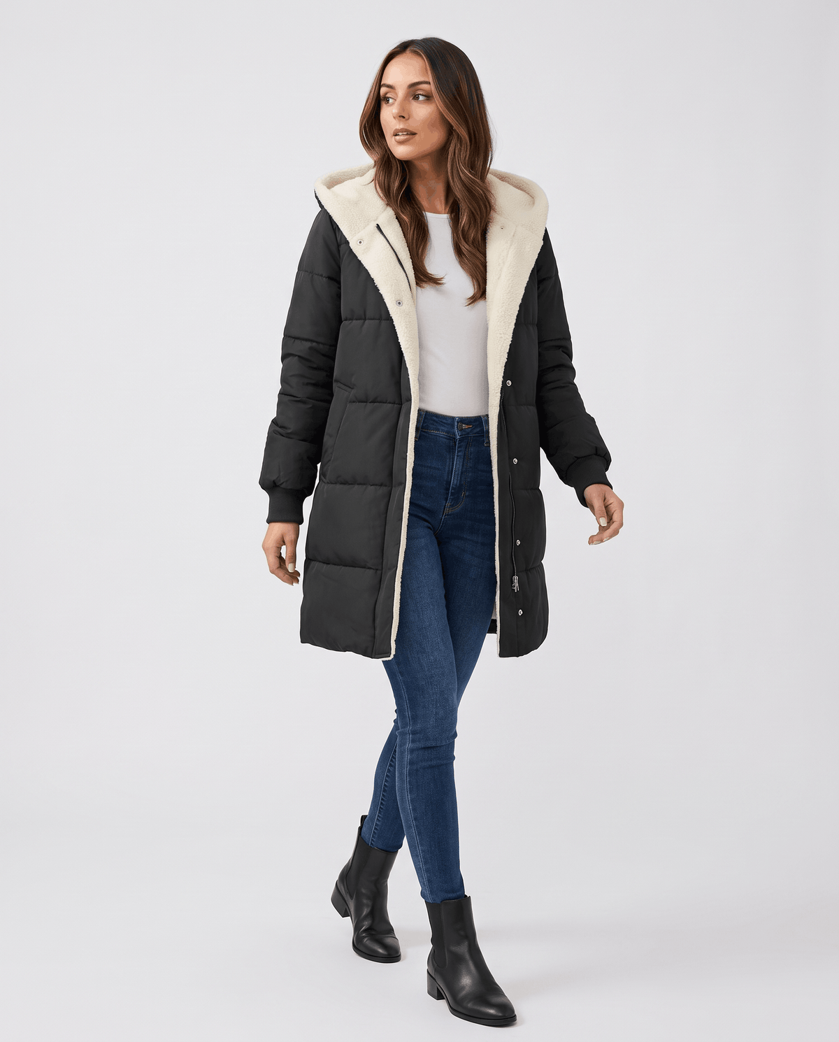 Model walking in black coat worn open over a white top and jeans