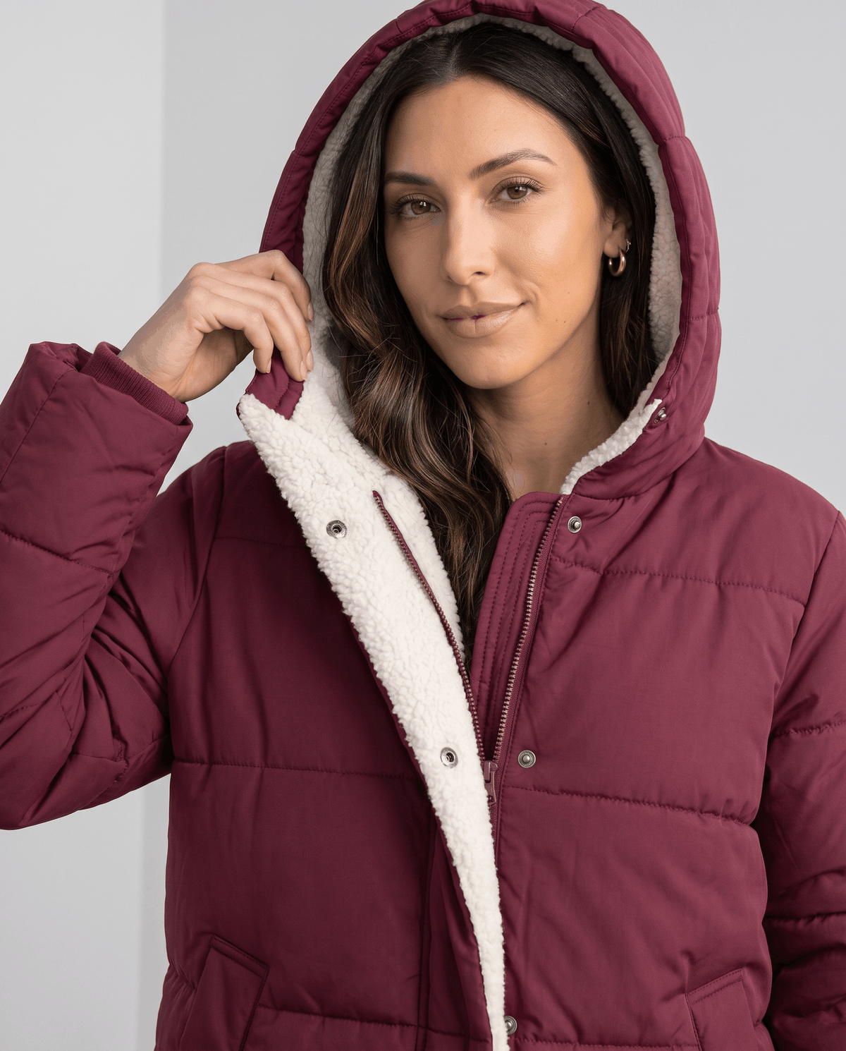 Model holding the sherpa-lined hood of a wine red puffer coat