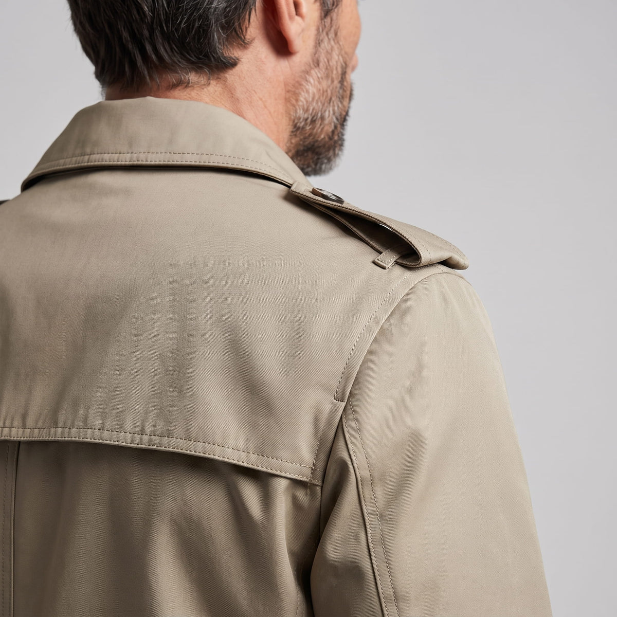 Close-up of beige trench coat shoulder with epaulet and storm yoke from behind