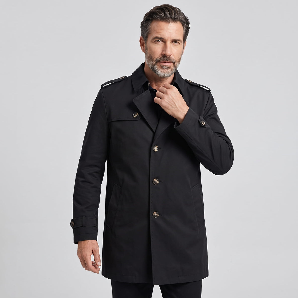Three-quarter view of black trench coat buttoned up with hand at collar
