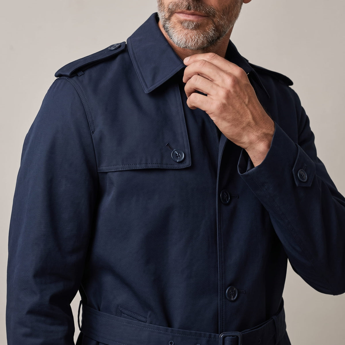 Close-up of navy trench coat collar and storm flap, model touching the collar