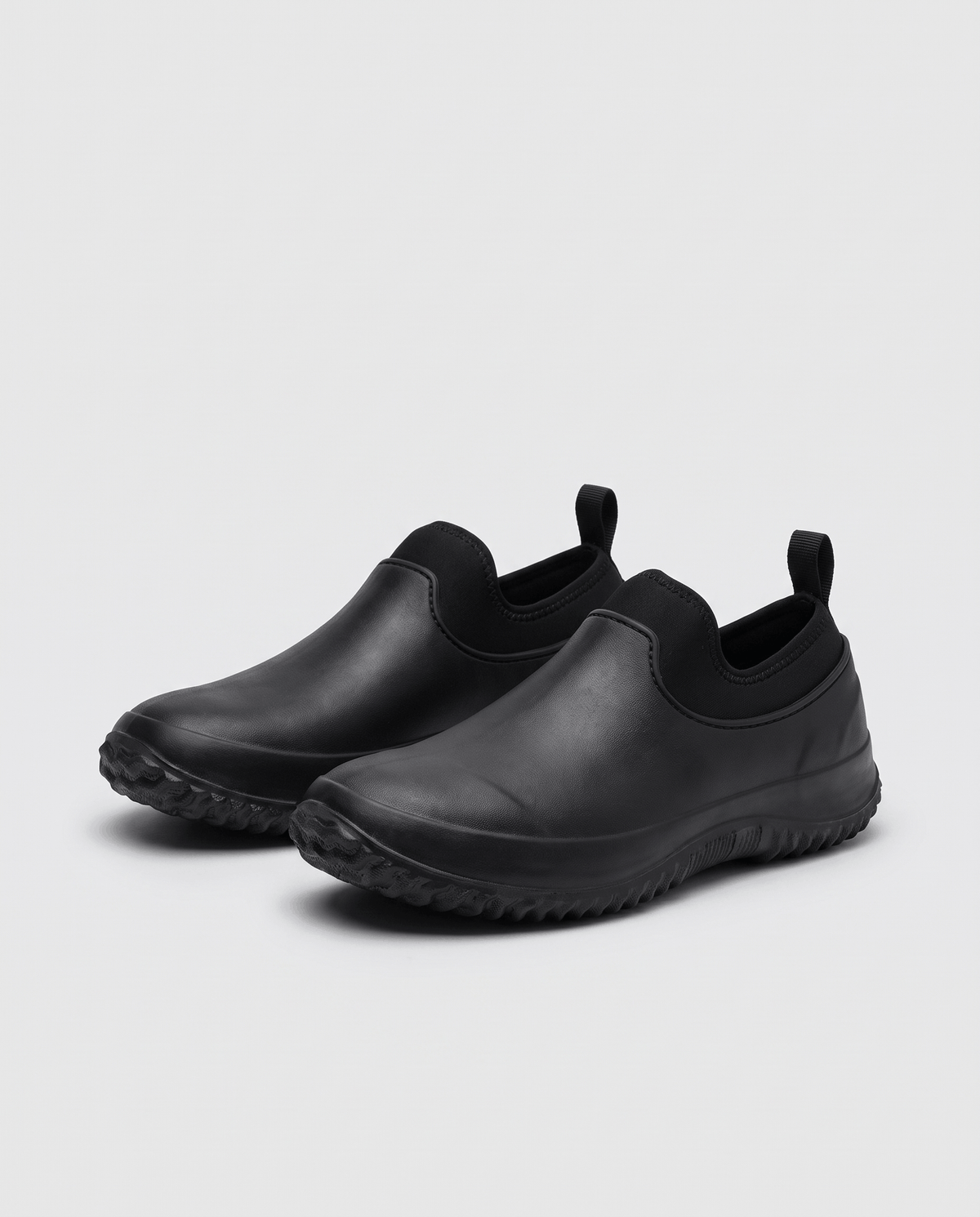 Pair of all-black slip-on shoes with stretch collars and pull loops on grey