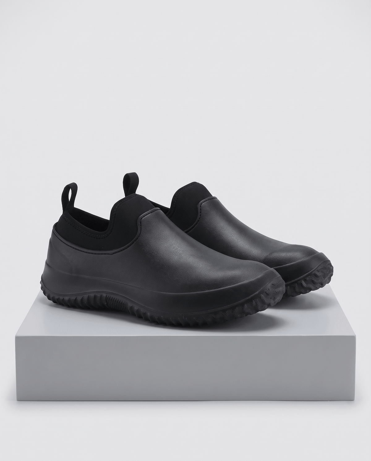 Two black shoes with pull loops displayed on a grey block