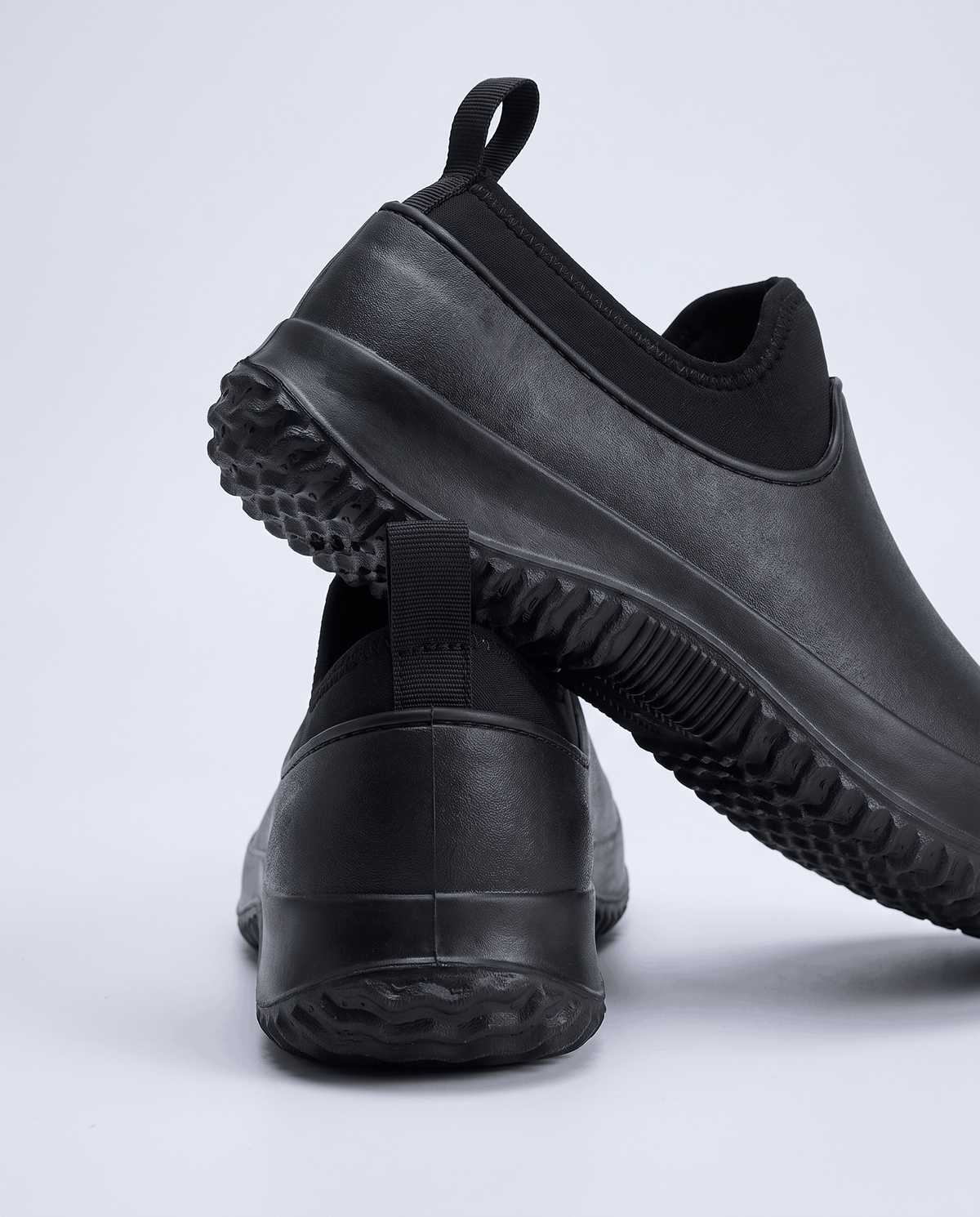 Black shoes with deep tread soles, one tilted to show the sole