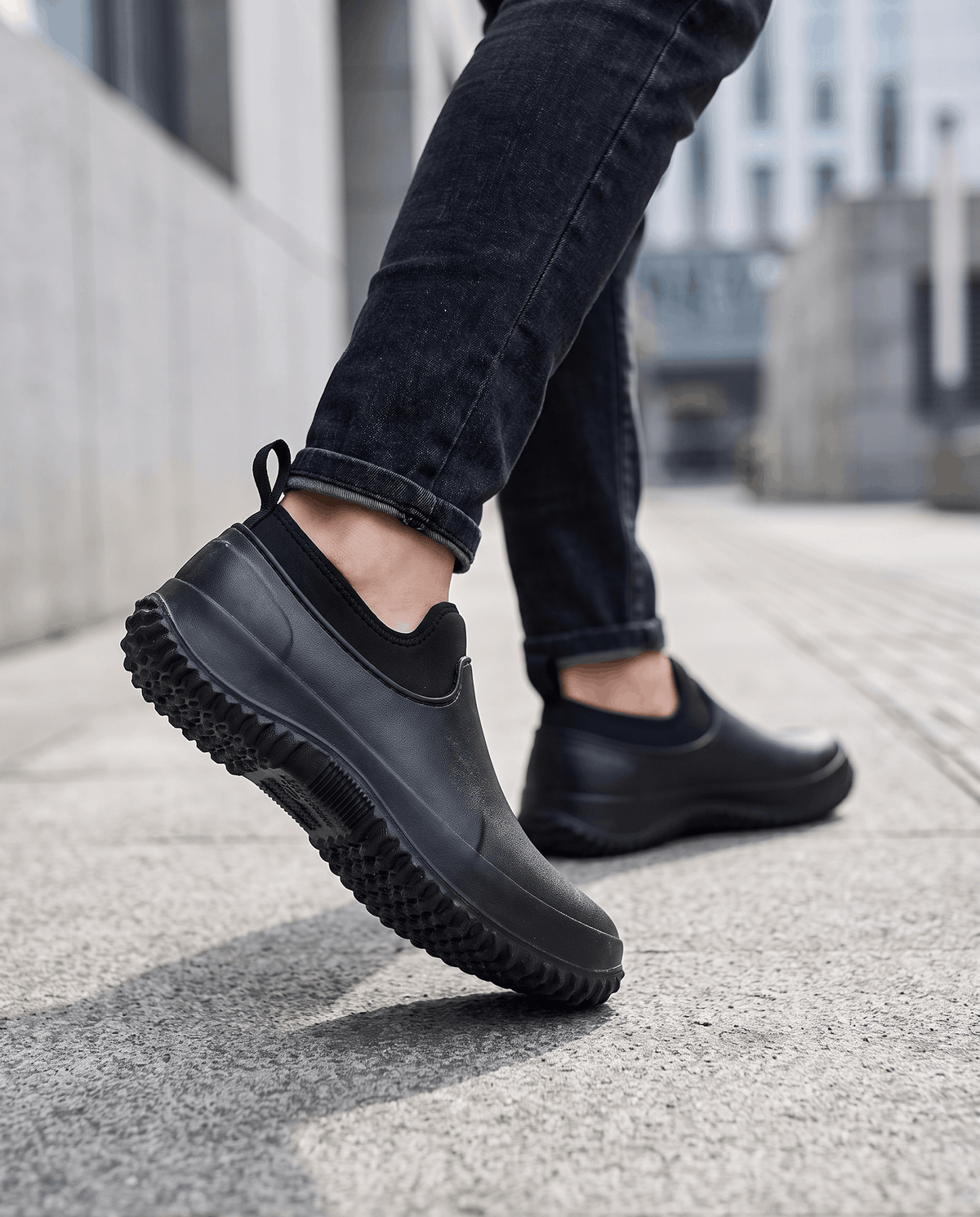 Legs in dark jeans walking in black slip-on shoes on a city sidewalk