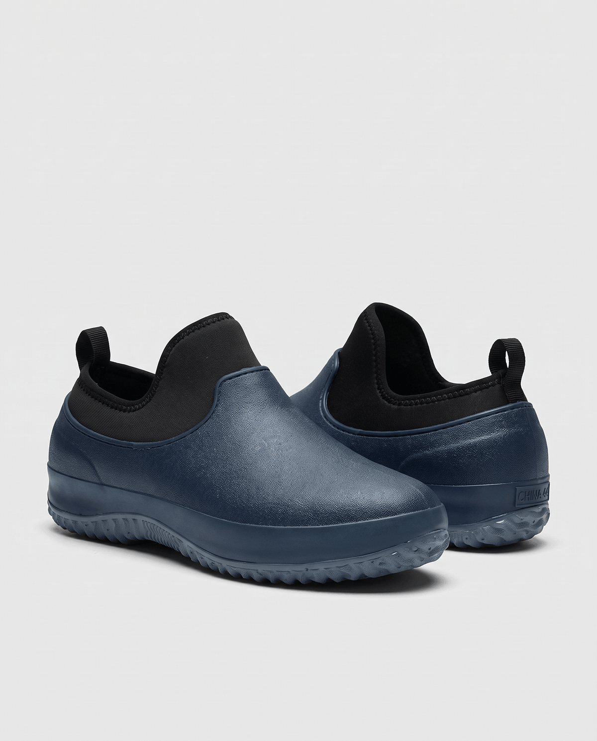 Two navy blue shoes with black collars and deep tread soles on a grey backdrop