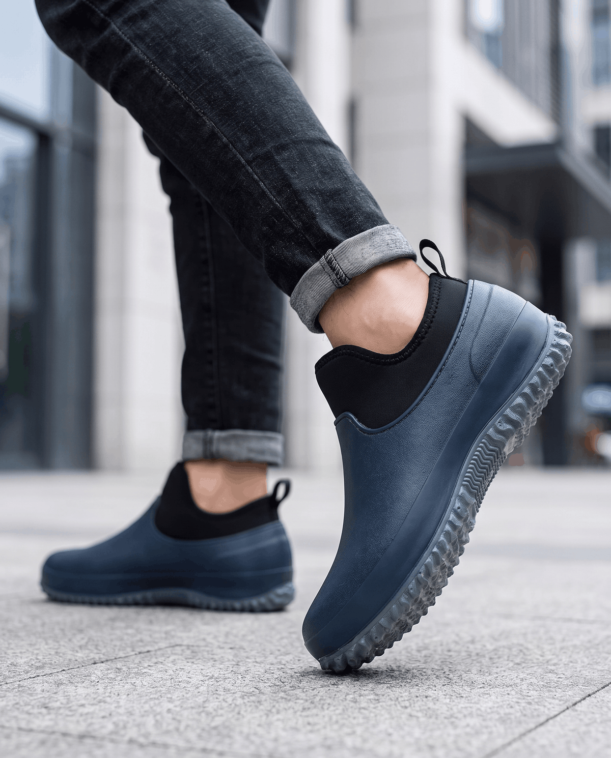 Legs in dark jeans walking in navy blue slip-on shoes on a city sidewalk
