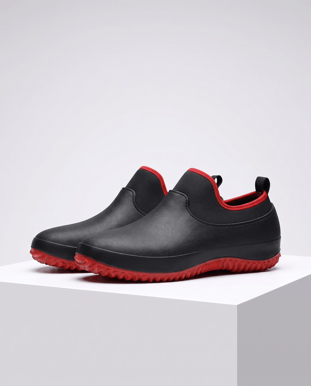 Pair of black shoes with red trim and red sole on a white block