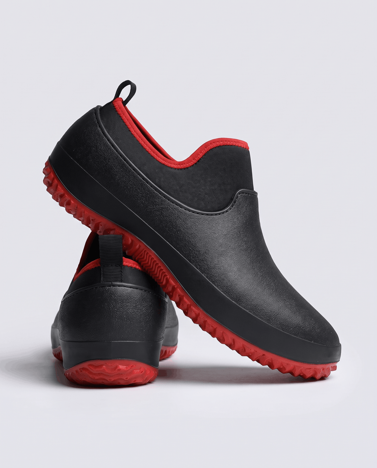 Black shoes with red trim and red tread sole, one resting on the other