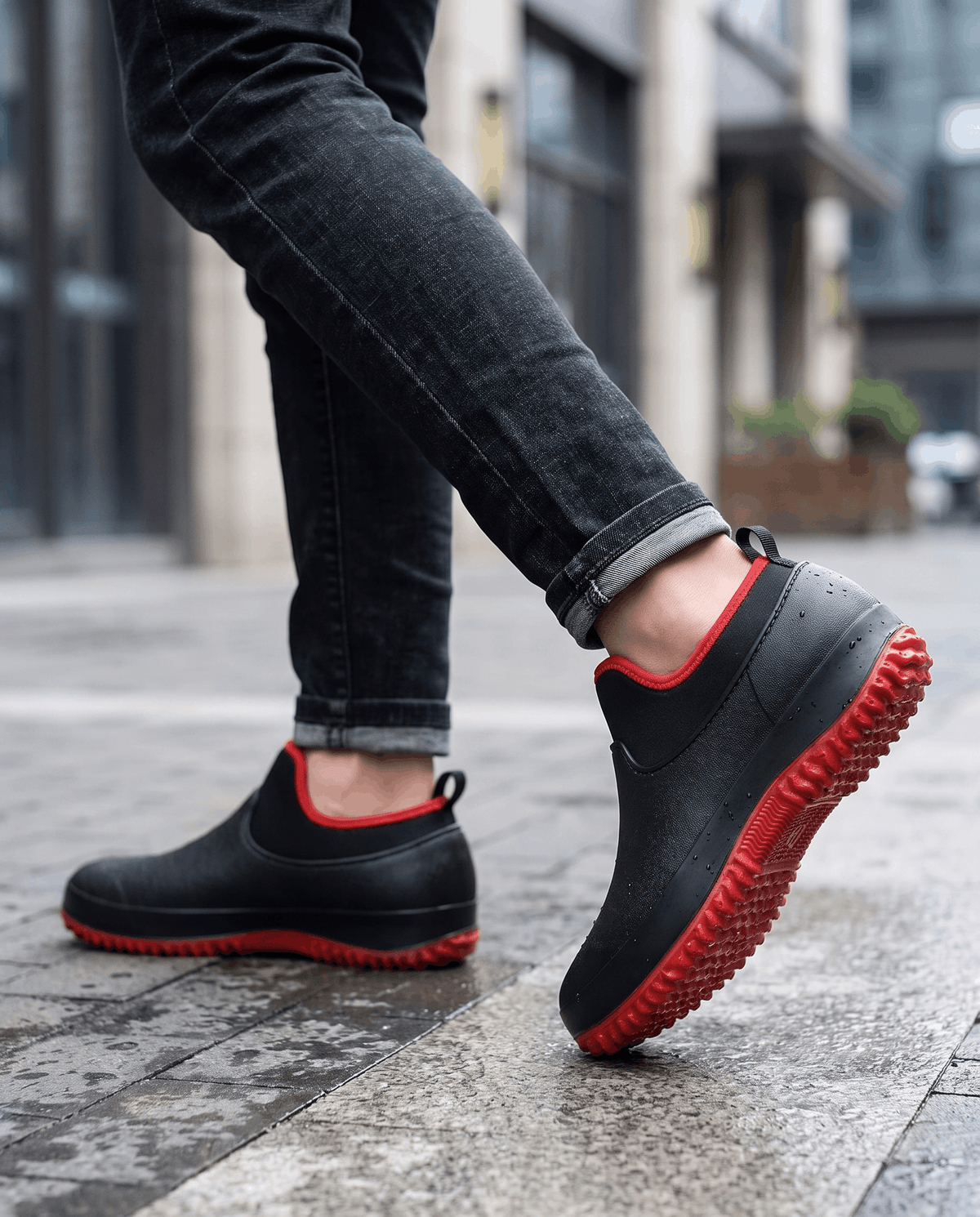 Legs in dark jeans walking in black shoes with red trim on a city sidewalk