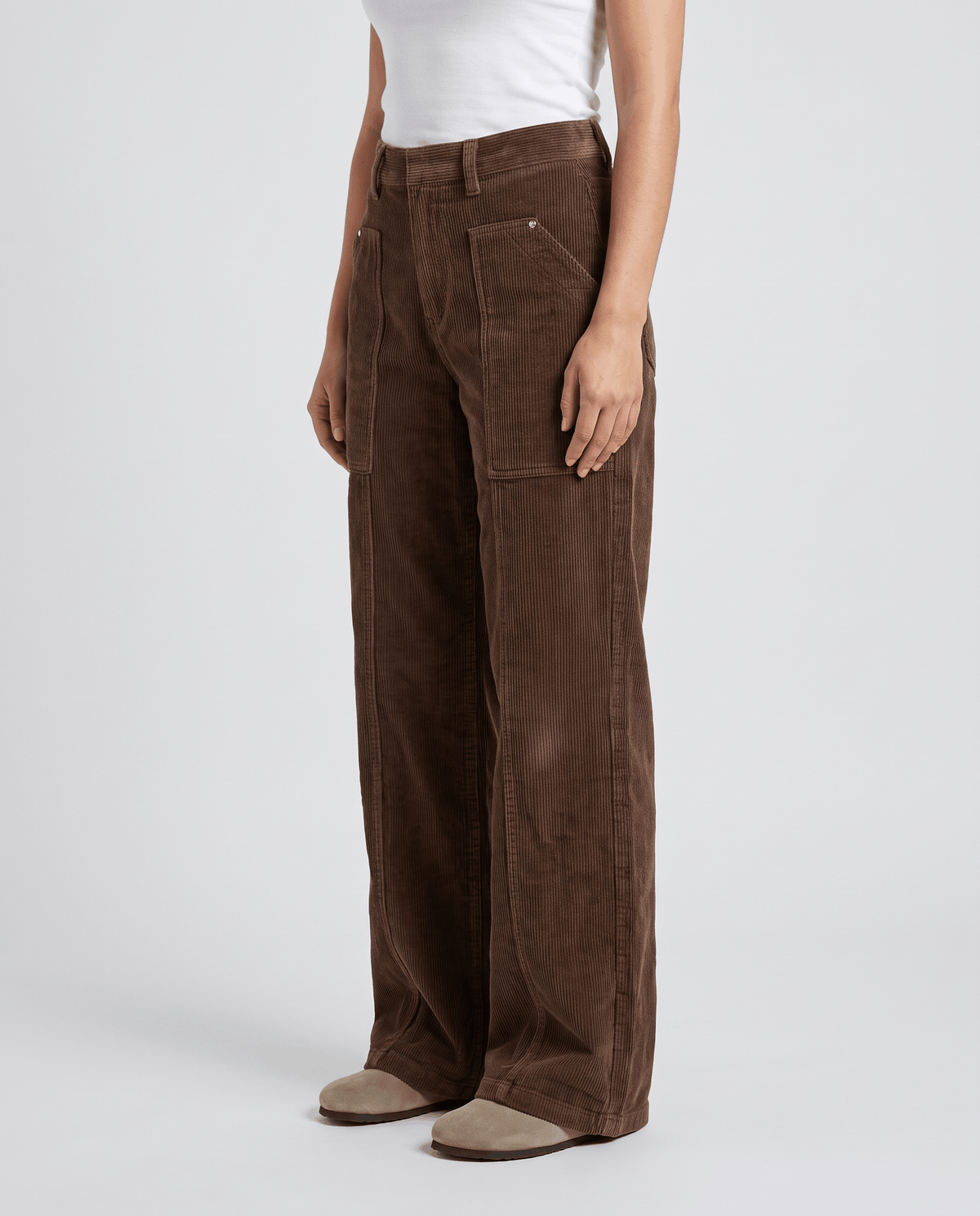 Angled front view of chocolate ribbed trousers with front patch pockets and suede shoes