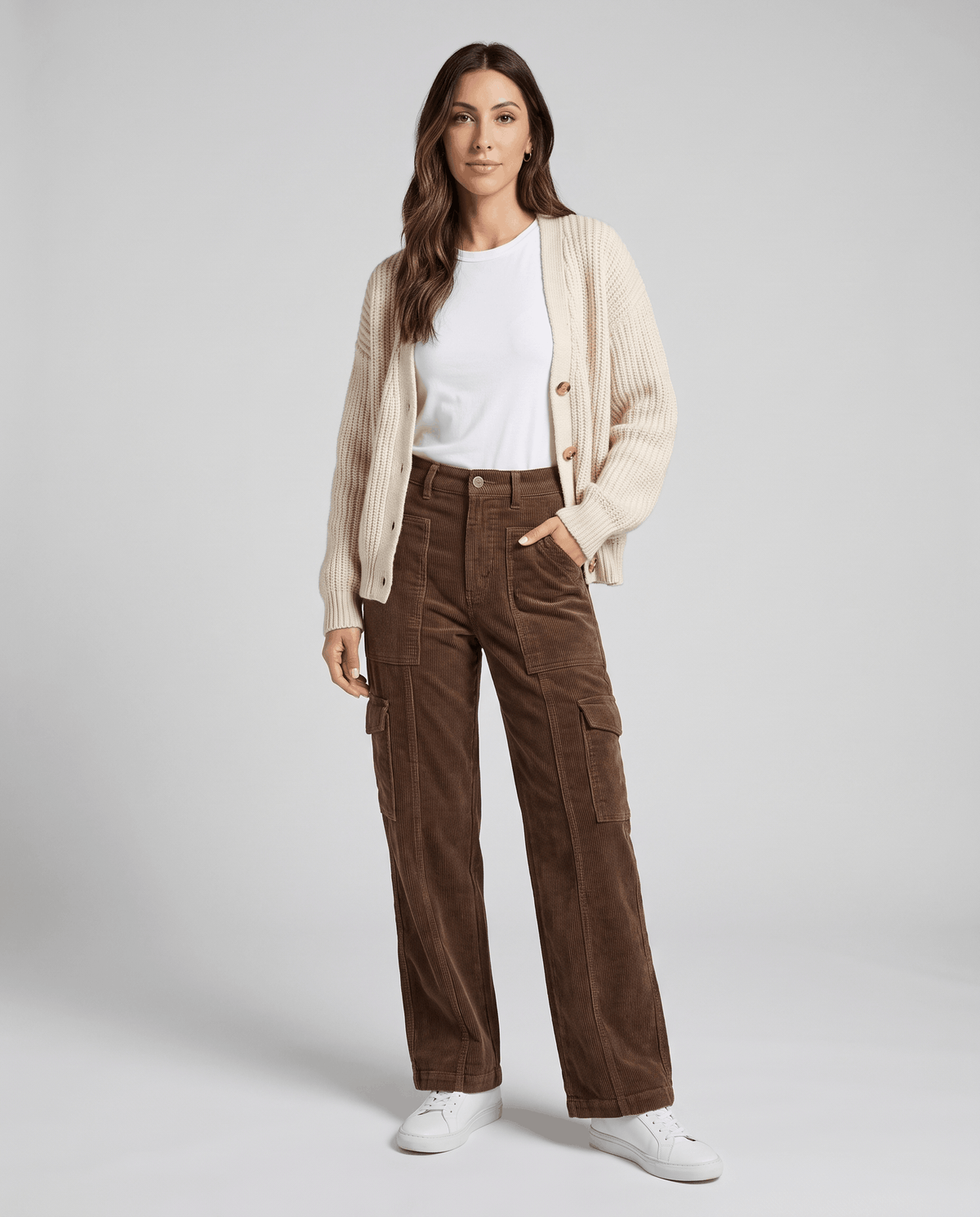 Model in brown ribbed pants styled with a cream cardigan, white tee and white sneakers