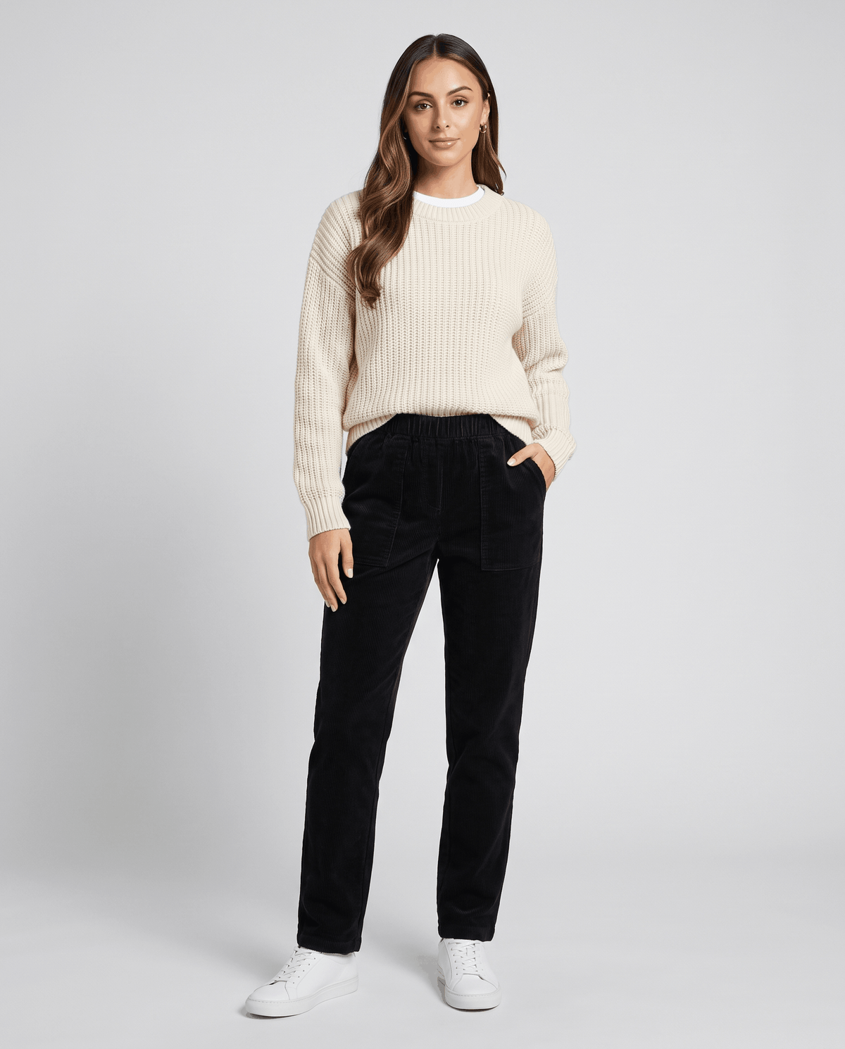 Model in black ribbed trousers styled with a cream knit sweater and white sneakers