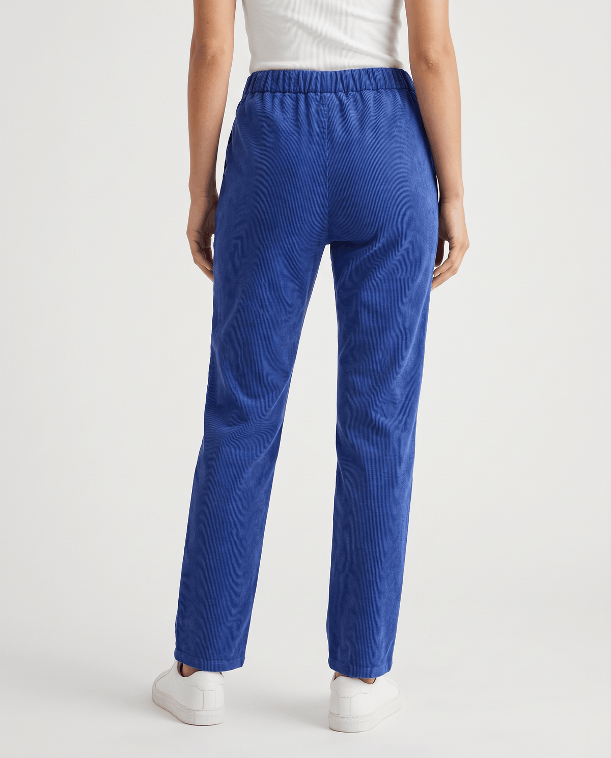 Back view of blue straight-leg trousers ending at the ankle, worn with white sneakers