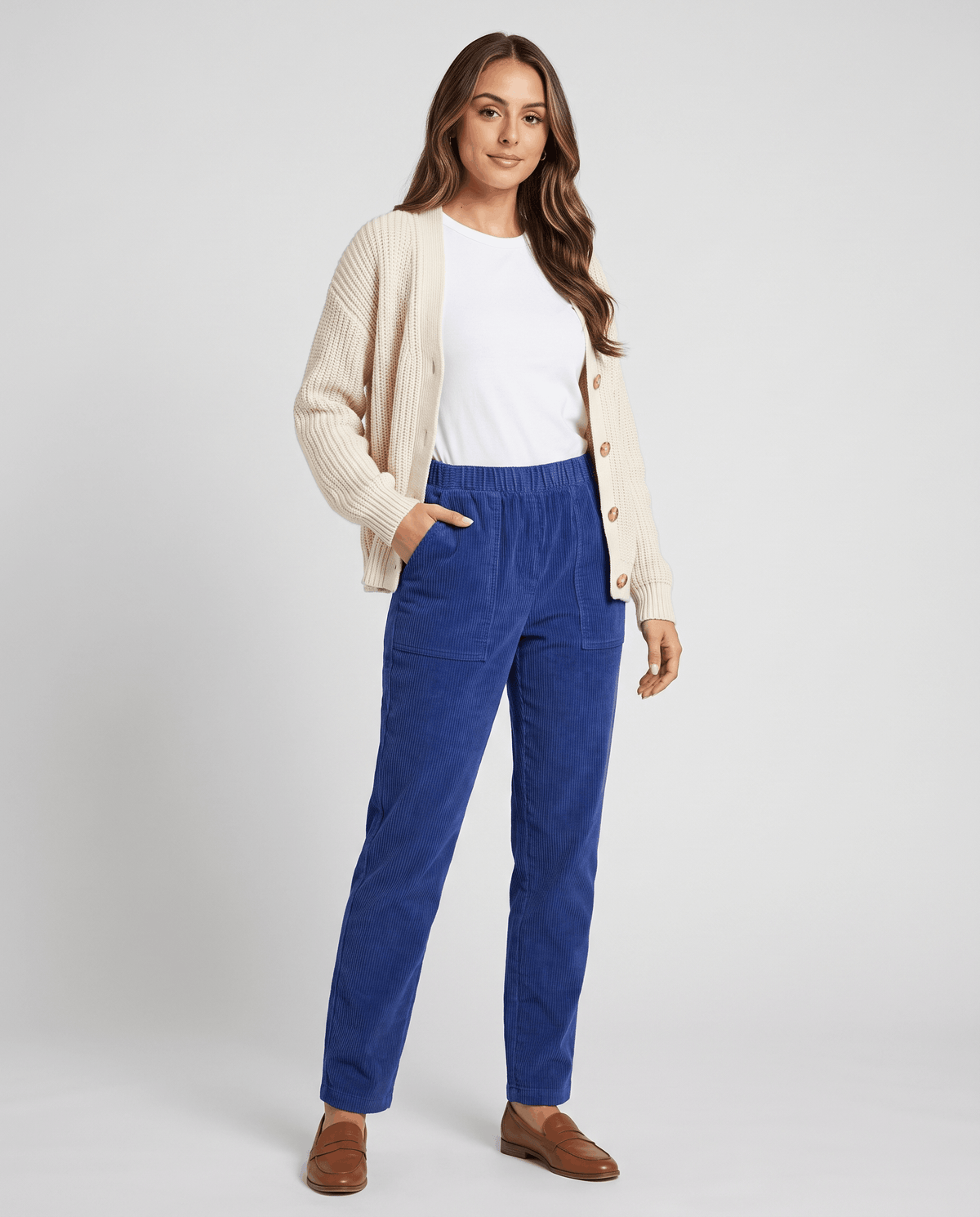 Model in blue ribbed trousers styled with a cream cardigan, white tee and brown loafers