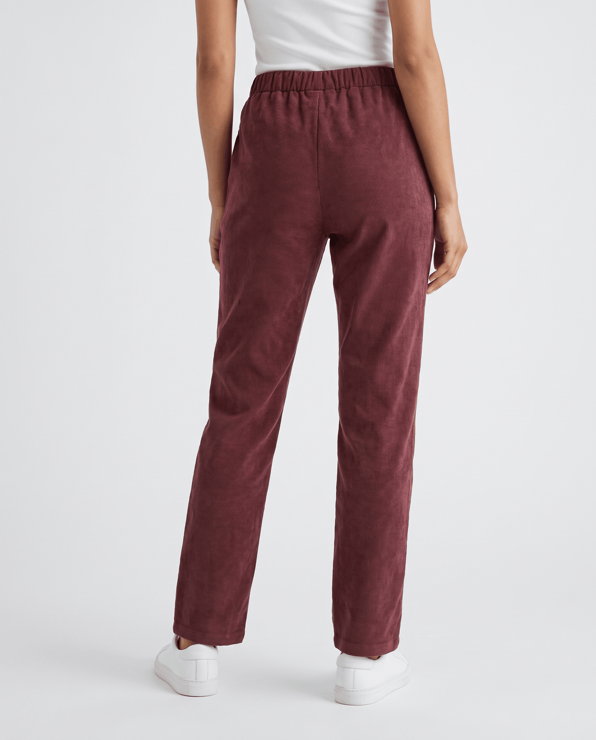 Back view of wine-colored ribbed trousers with an elastic waistband, worn with white sneakers