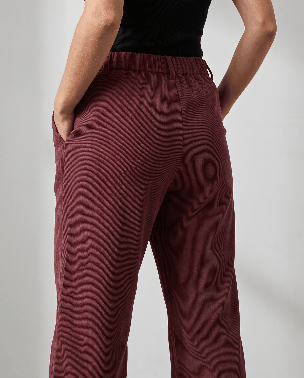 Side-back close-up of deep red ribbed pants at the hip, worn with a black top