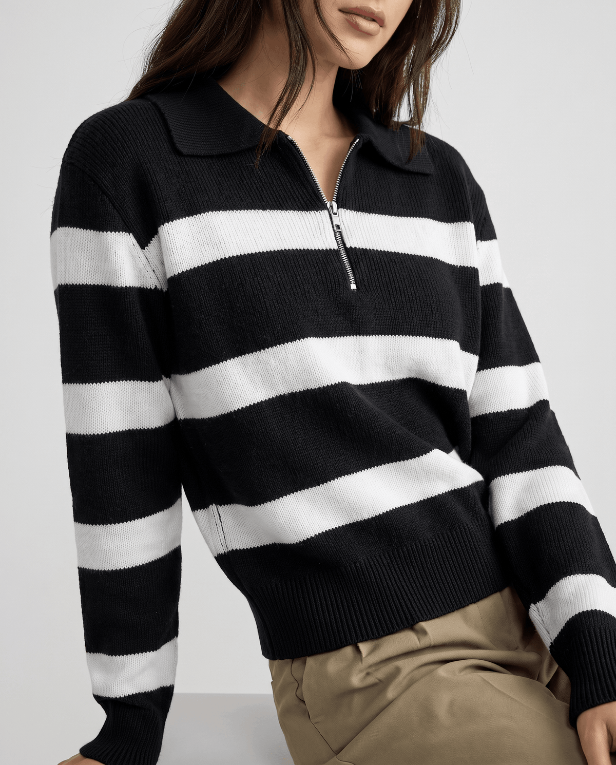Cropped view of black striped knit pullover worn with khaki pants, seated pose