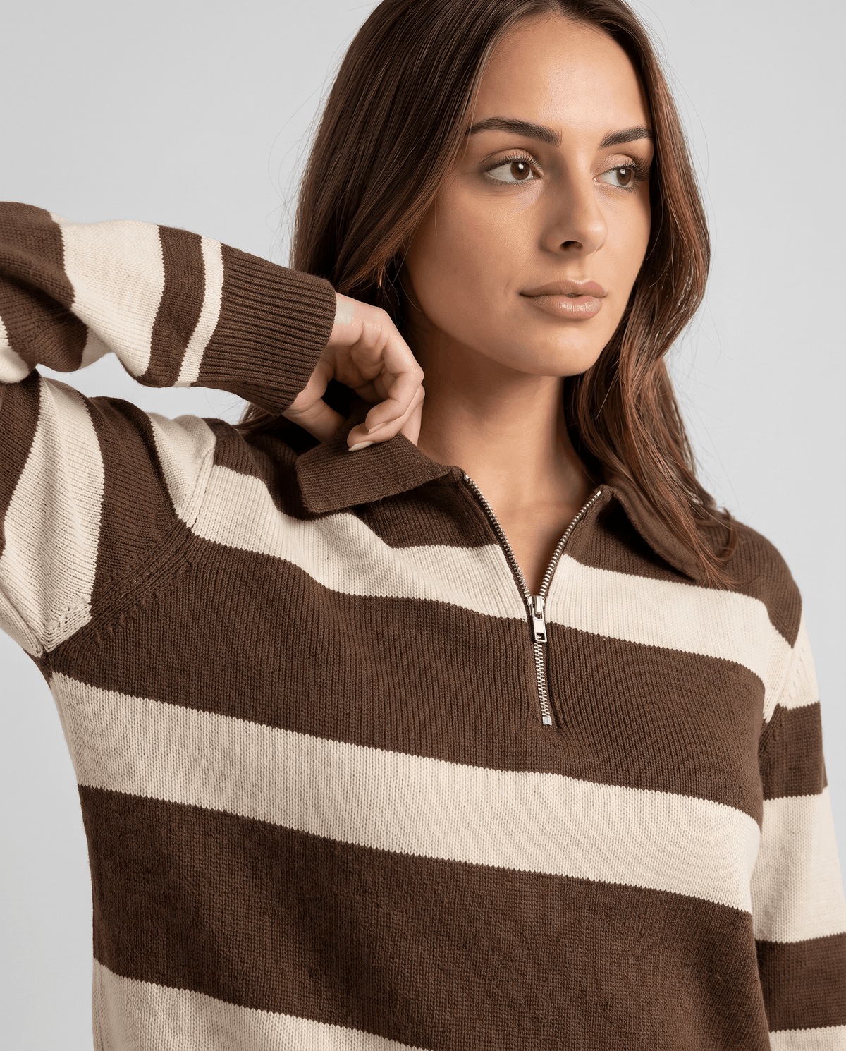 Model adjusting the collar of a brown and cream striped zip-neck sweater