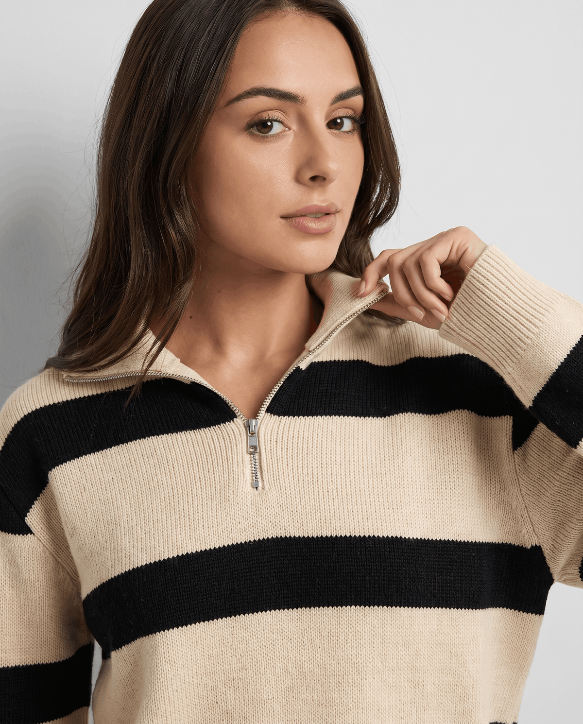 Close-up of model touching the polo collar and silver zip on a beige striped knit