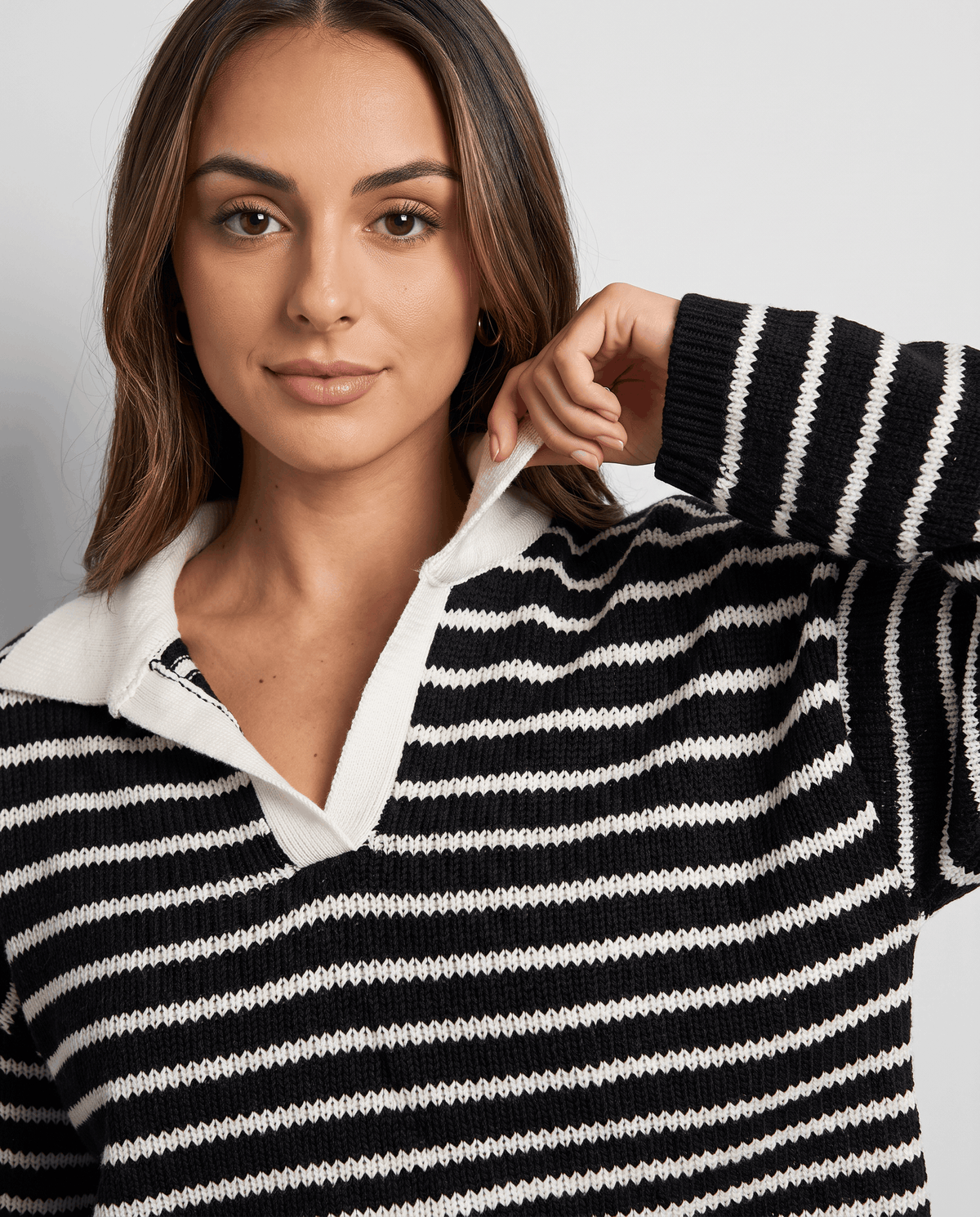 Woman adjusting the white collar of a black striped long-sleeve knit top