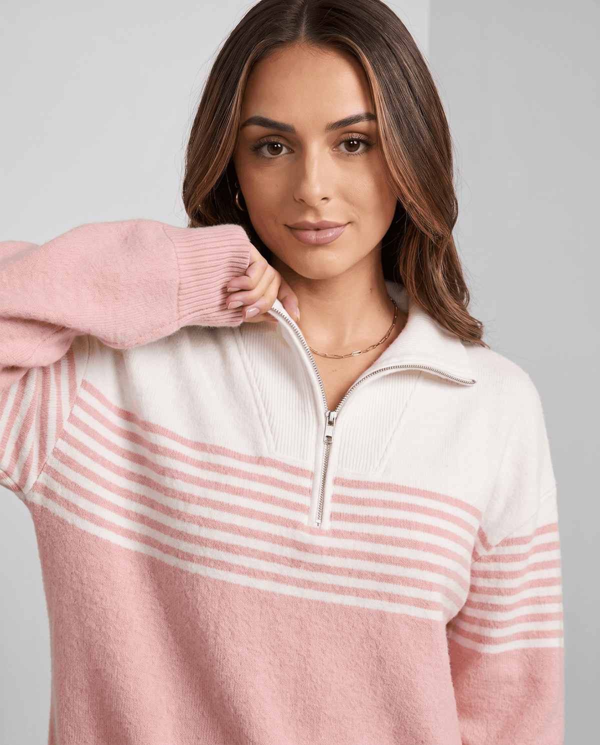 Model touching her hair in a light pink zip-neck pullover, showing collar and stripes