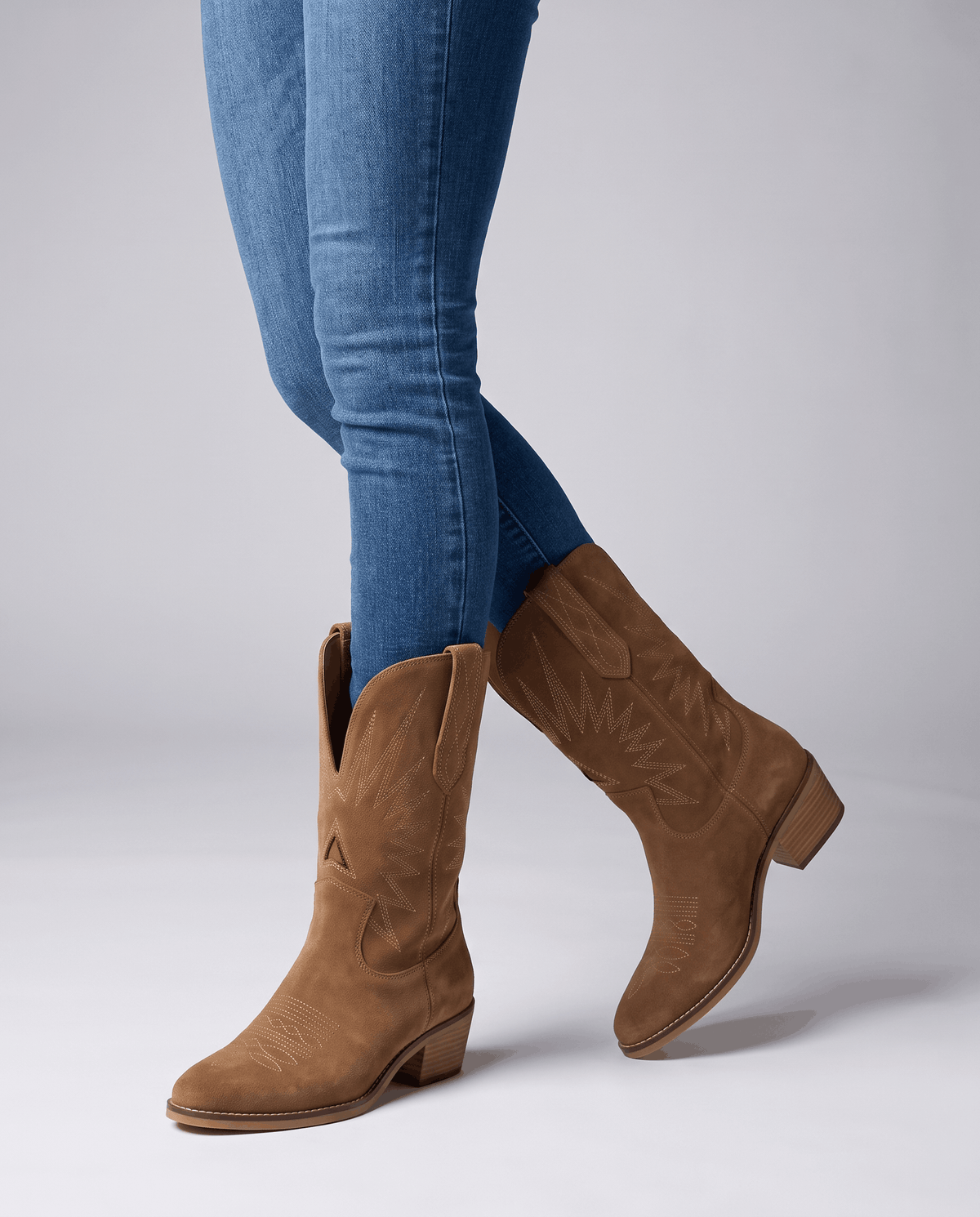 Studio shot of blue jeans worn over mid-calf suede boots with a stacked heel