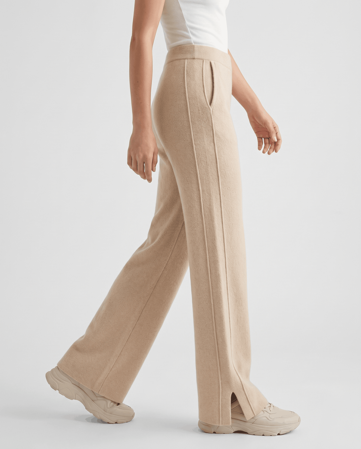 Beige knit pants in side view walking, front seam and hem slit visible