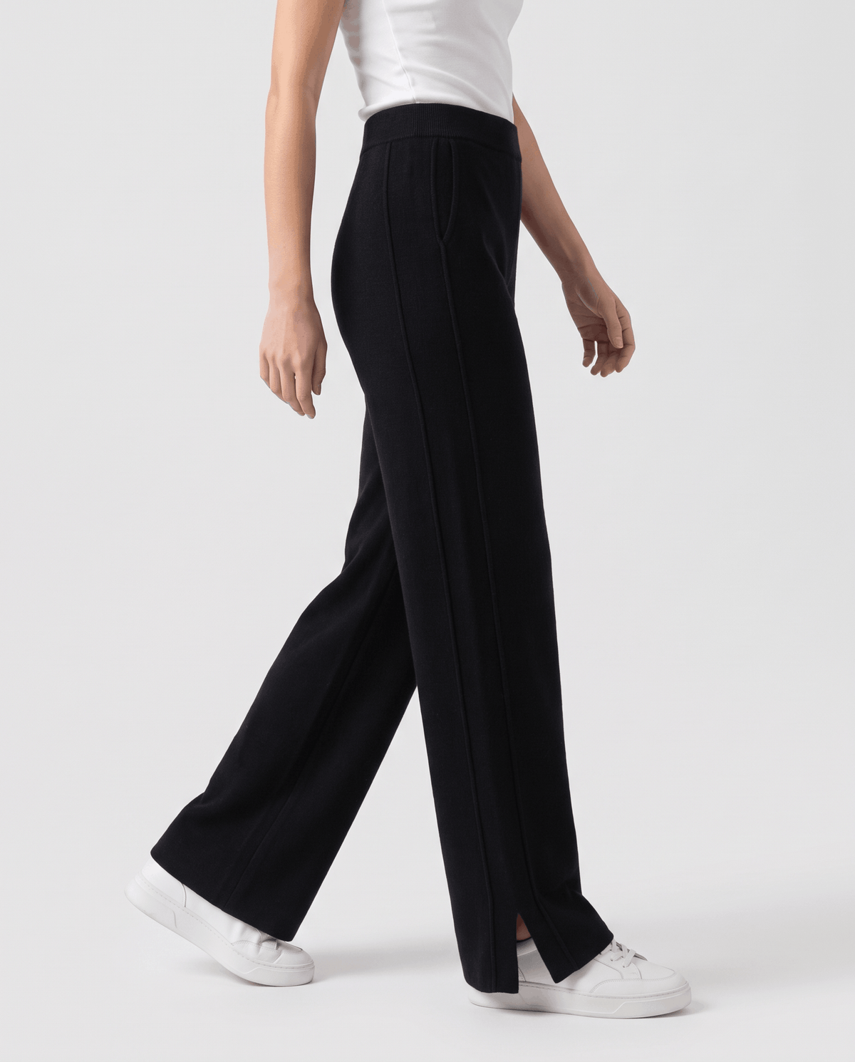 Black knit pants in side profile mid-stride, showing split side hem