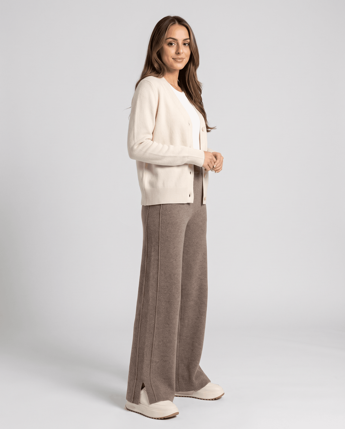 Model in cream cardigan and khaki wool pants standing three-quarter turned