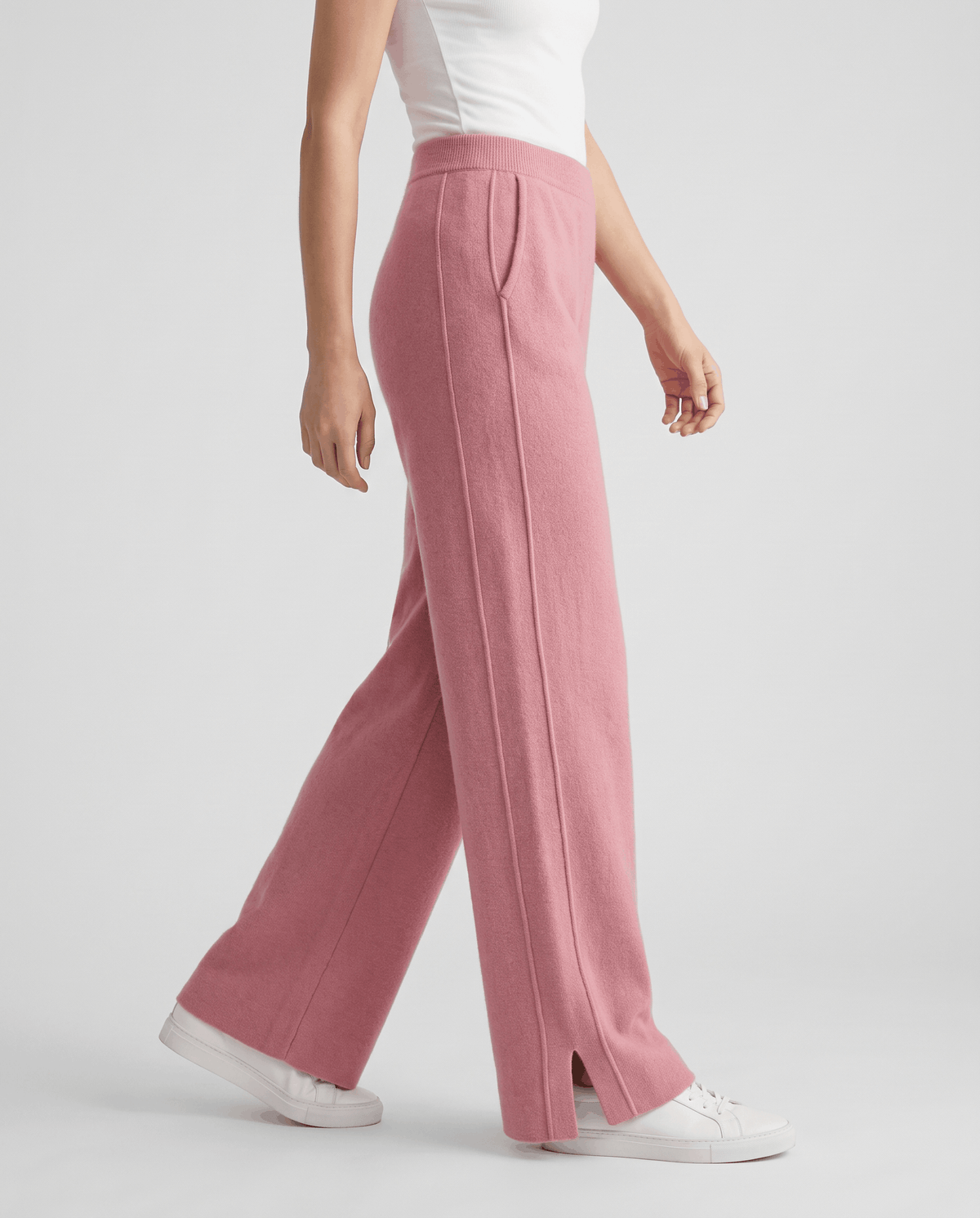 Pink knit pants in side view, front seam and split hem with white sneakers