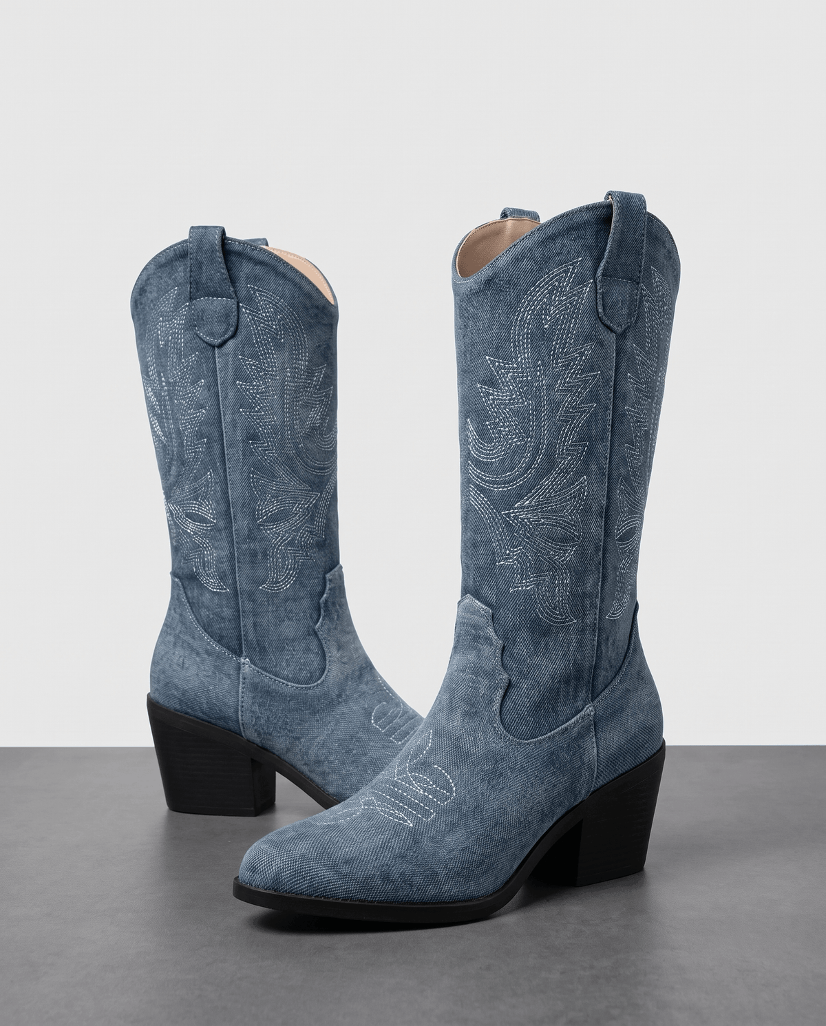 Pair of blue boots with decorative stitching standing against a grey studio backdrop