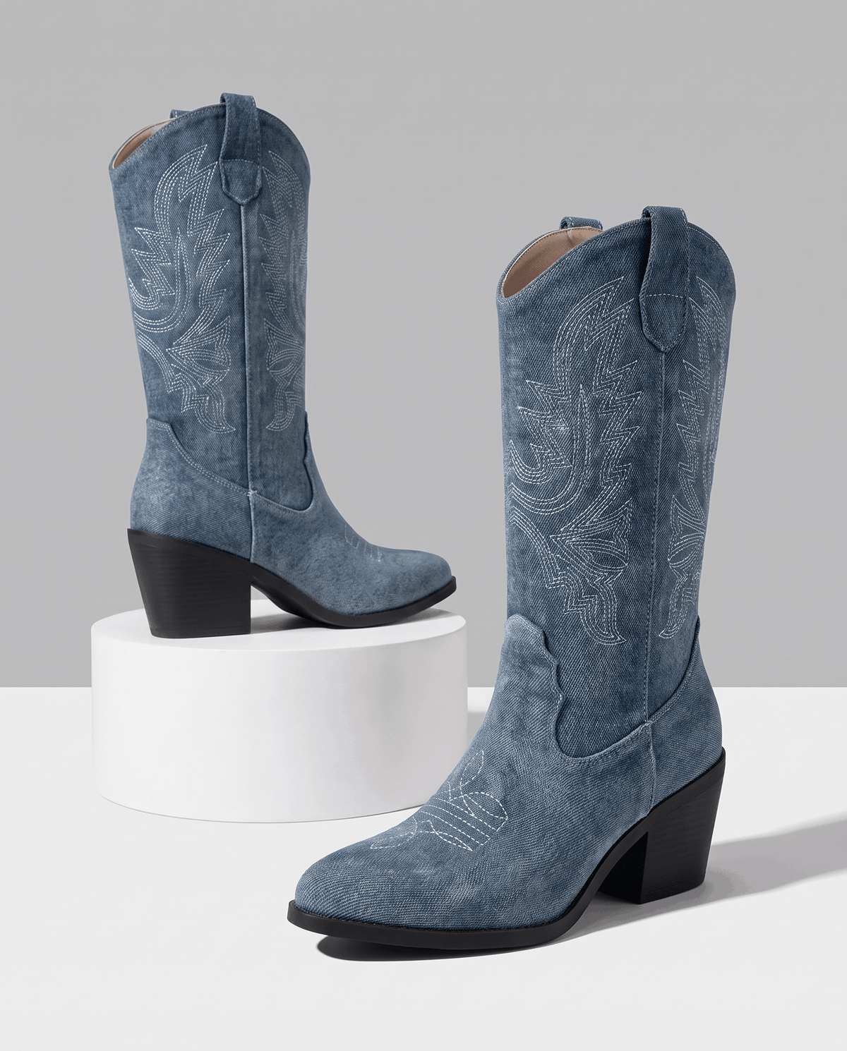 Two blue stitched boots with black block heels displayed on a white pedestal