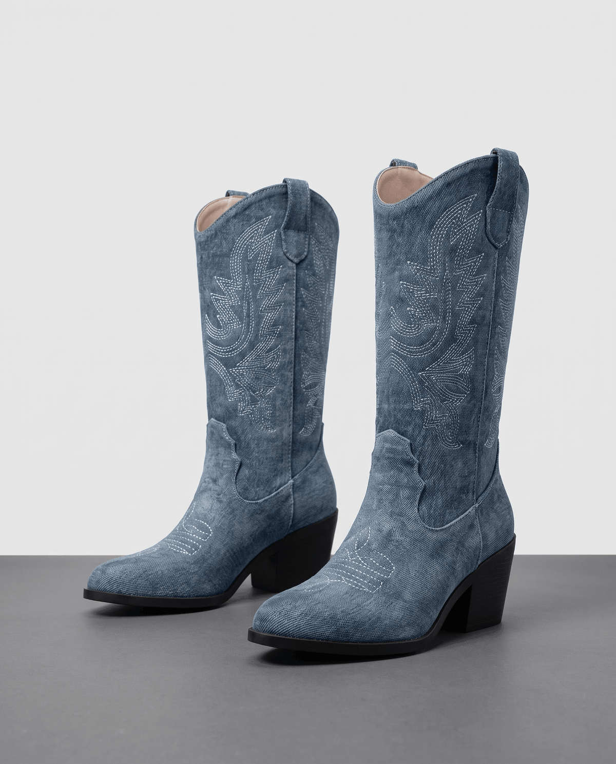 Pair of blue textured boots with stitched shafts and black block heels on a grey floor
