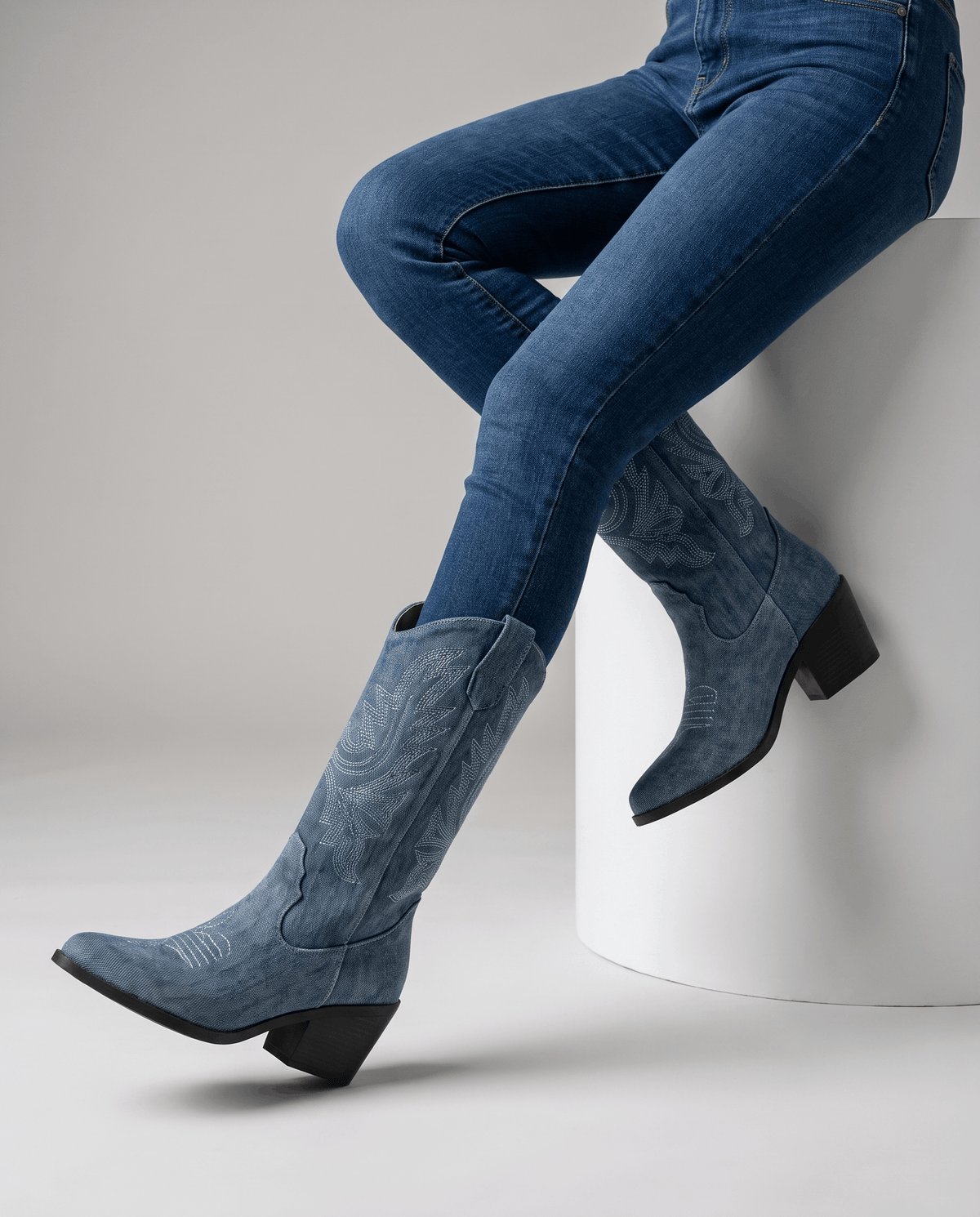 Seated legs in blue jeans and blue boots with pointed toes and black heels